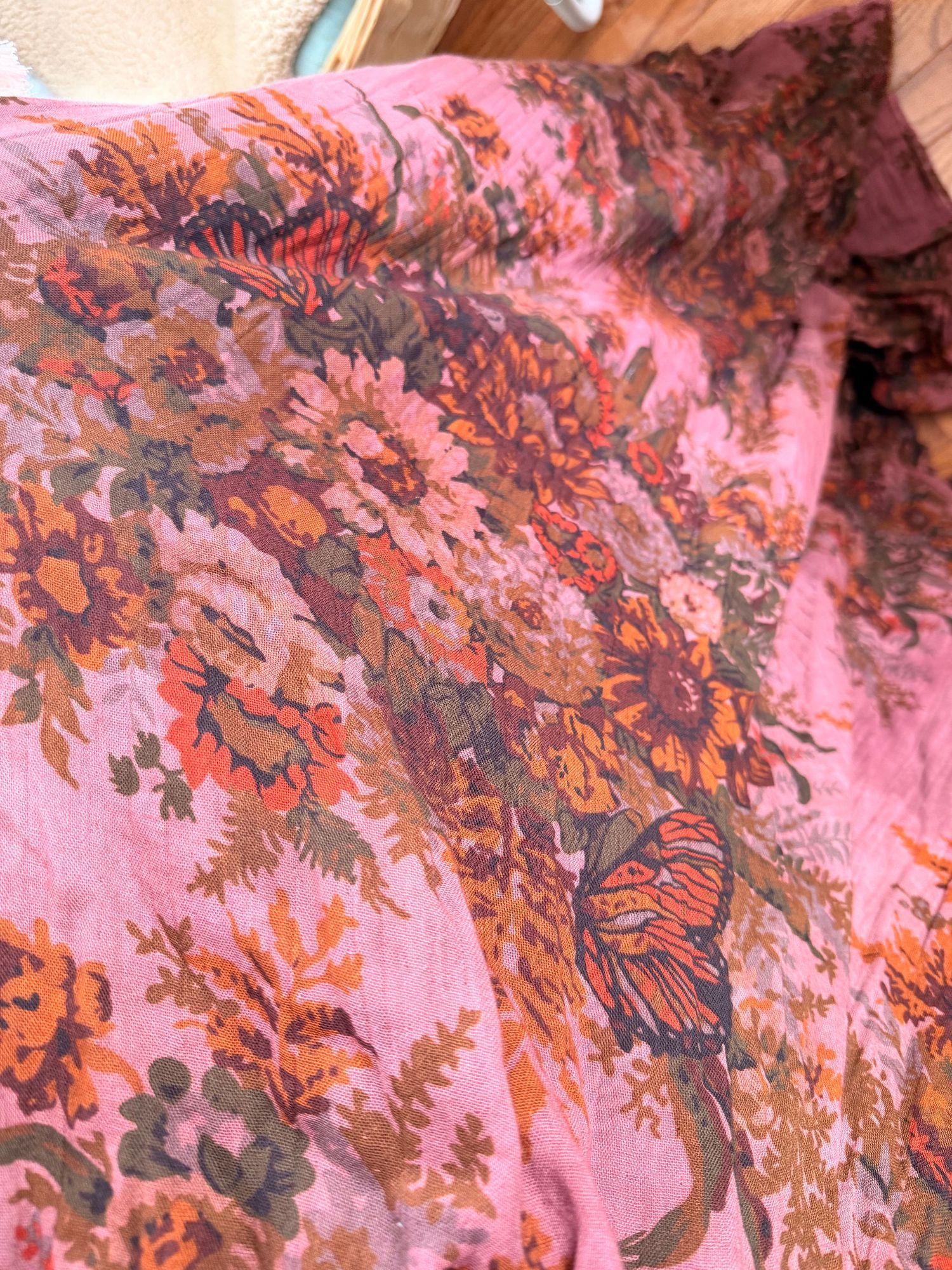 Pink floral fabric with orange and brown flowers and a butterfly print in a vintage bohemian style.