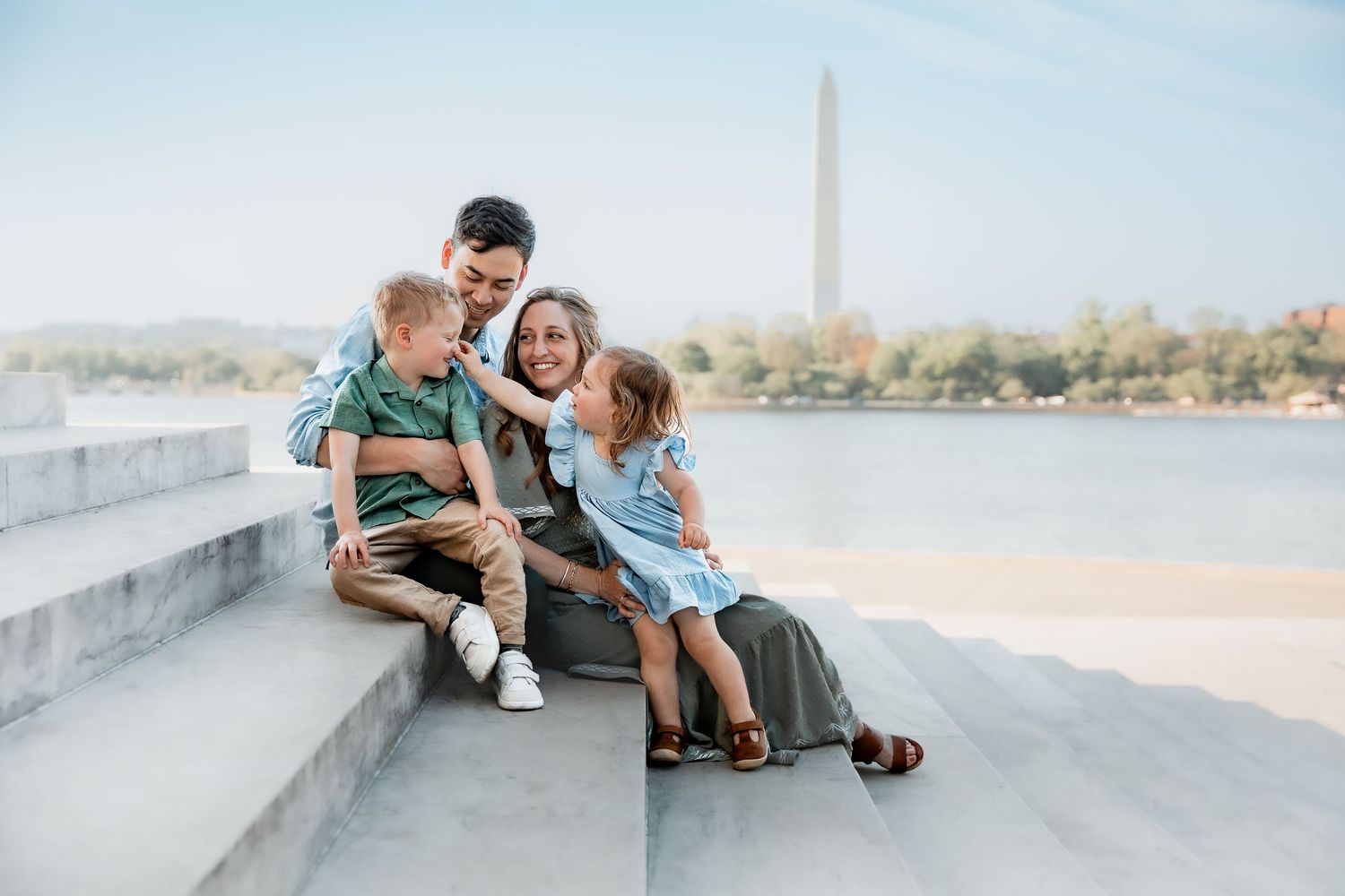 Family of four sitting on marble steps near the Washington Monument, sharing a joyful moment by the Tidal Basin.