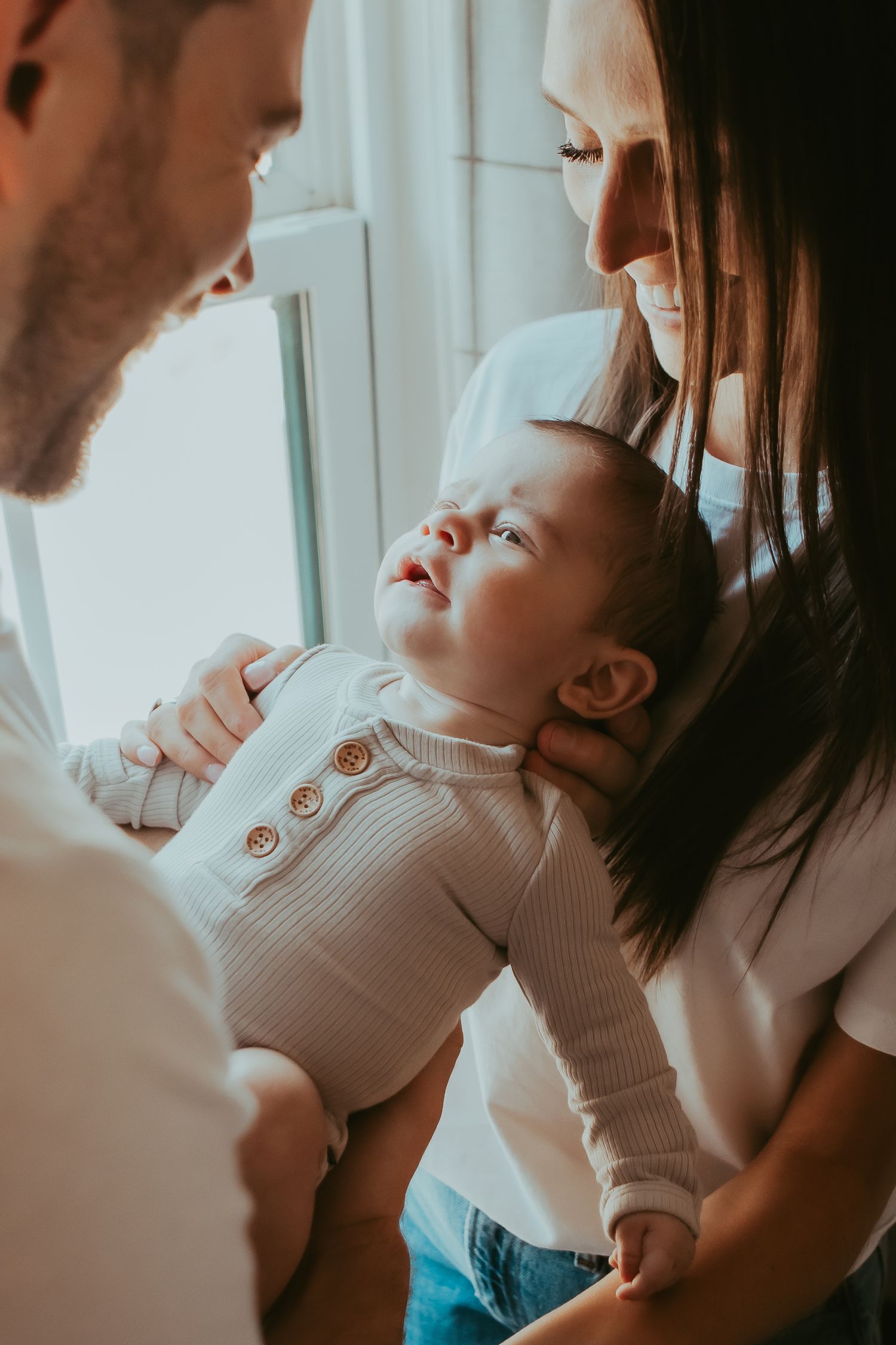 Family sharing an intimate moment together near a bright window with soft lighting.