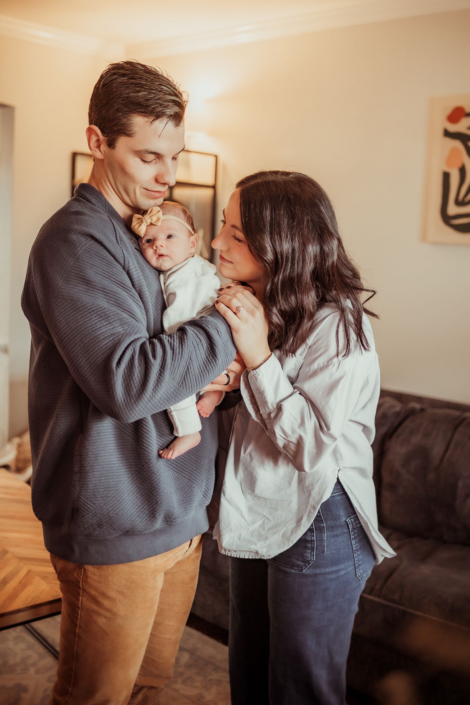 A tender family moment in a warmly lit living room with neutral decor and casual attire.