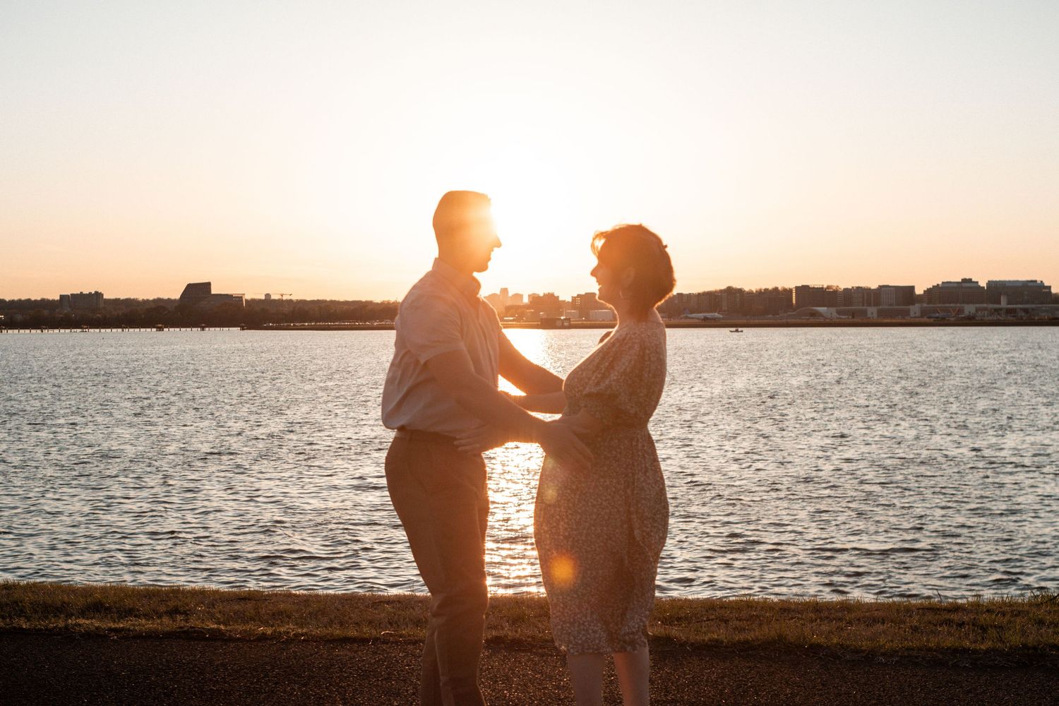 A romantic silhouette of a couple embracing by the water during sunset with a glowing golden sky in the background.