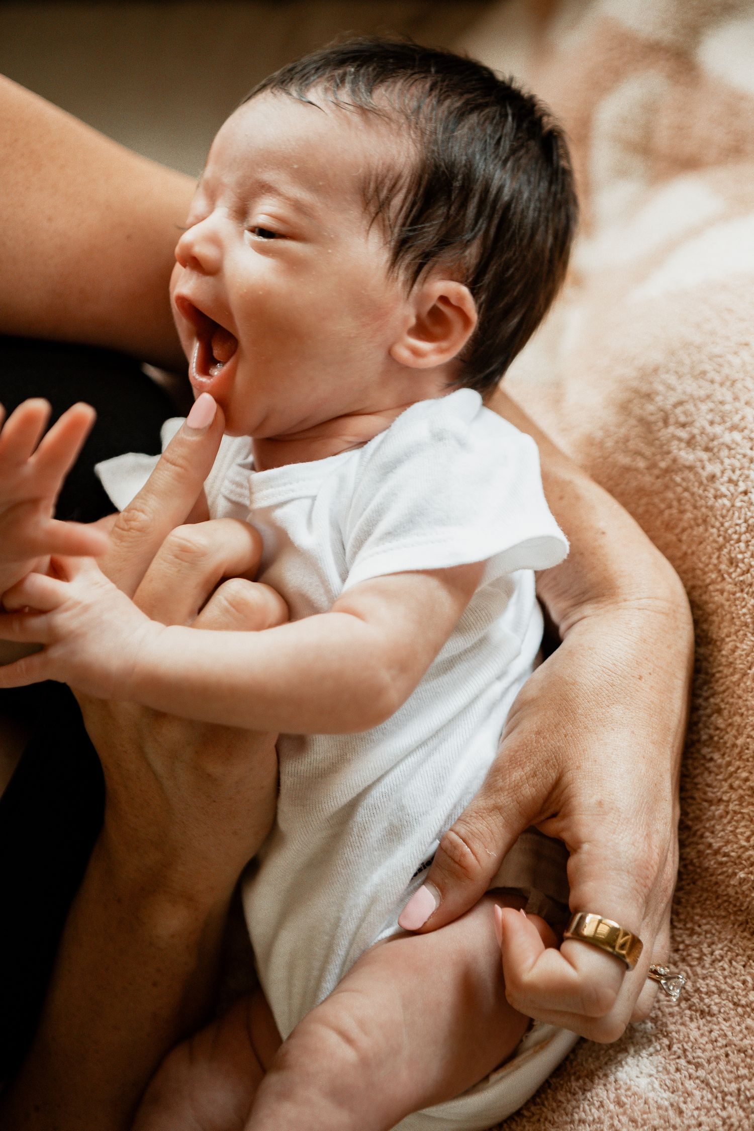 A tender series showing a baby in white clothing being held and cuddled against warm textured fabric.