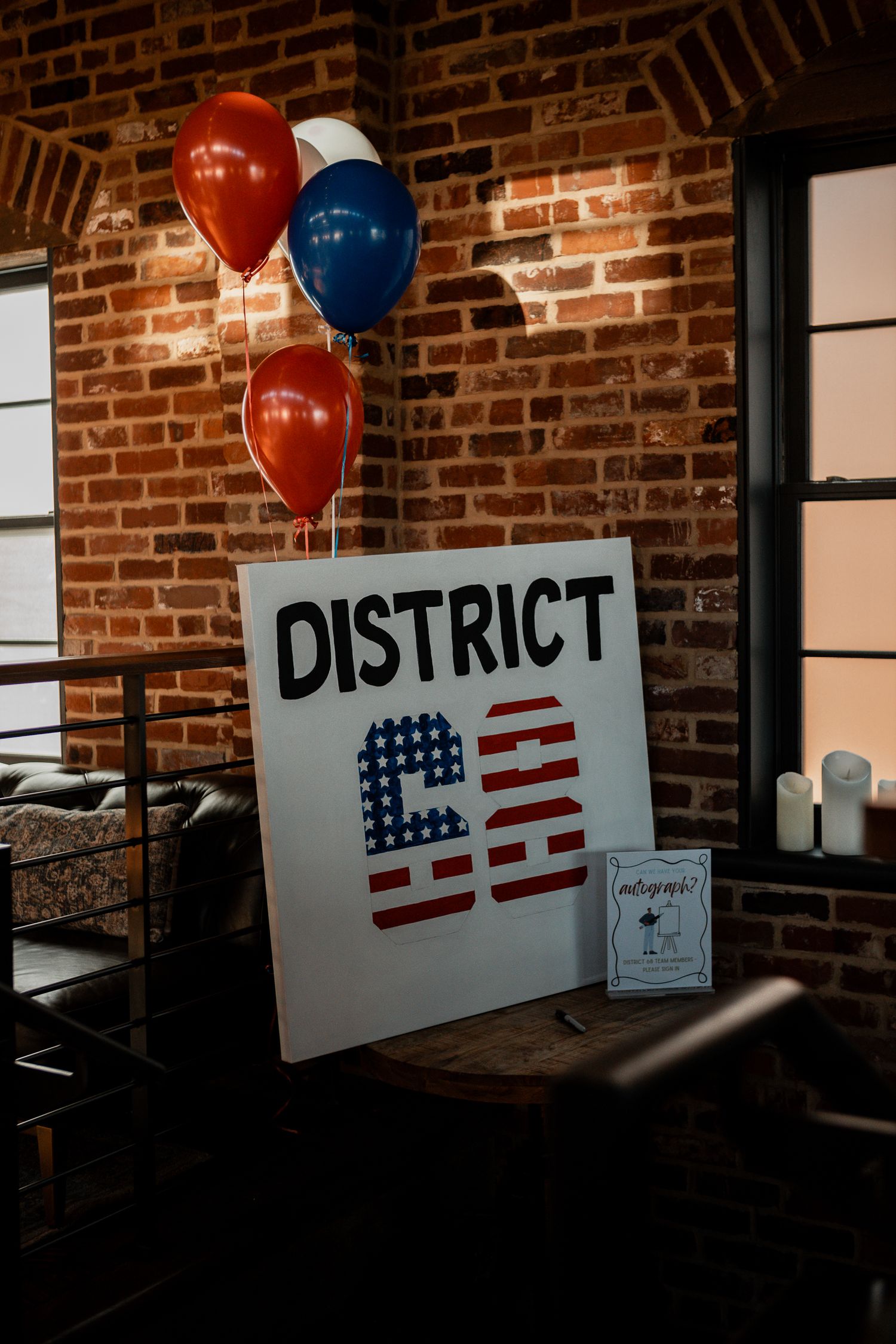 District-themed signage with patriotic design and red and blue balloons against brick wall.