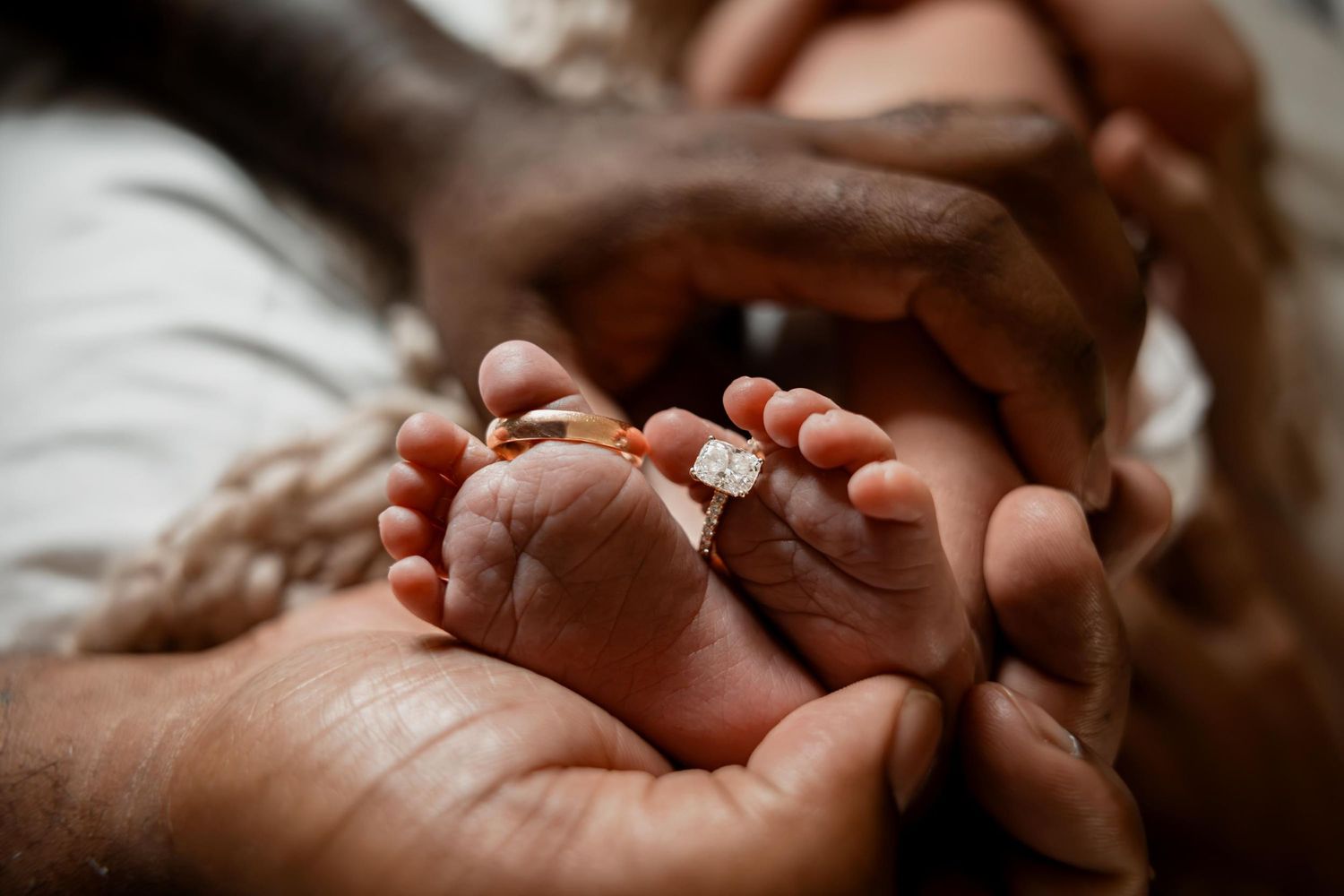 Newborn baby feet adorned with parents wedding rings held gently in loving hands.