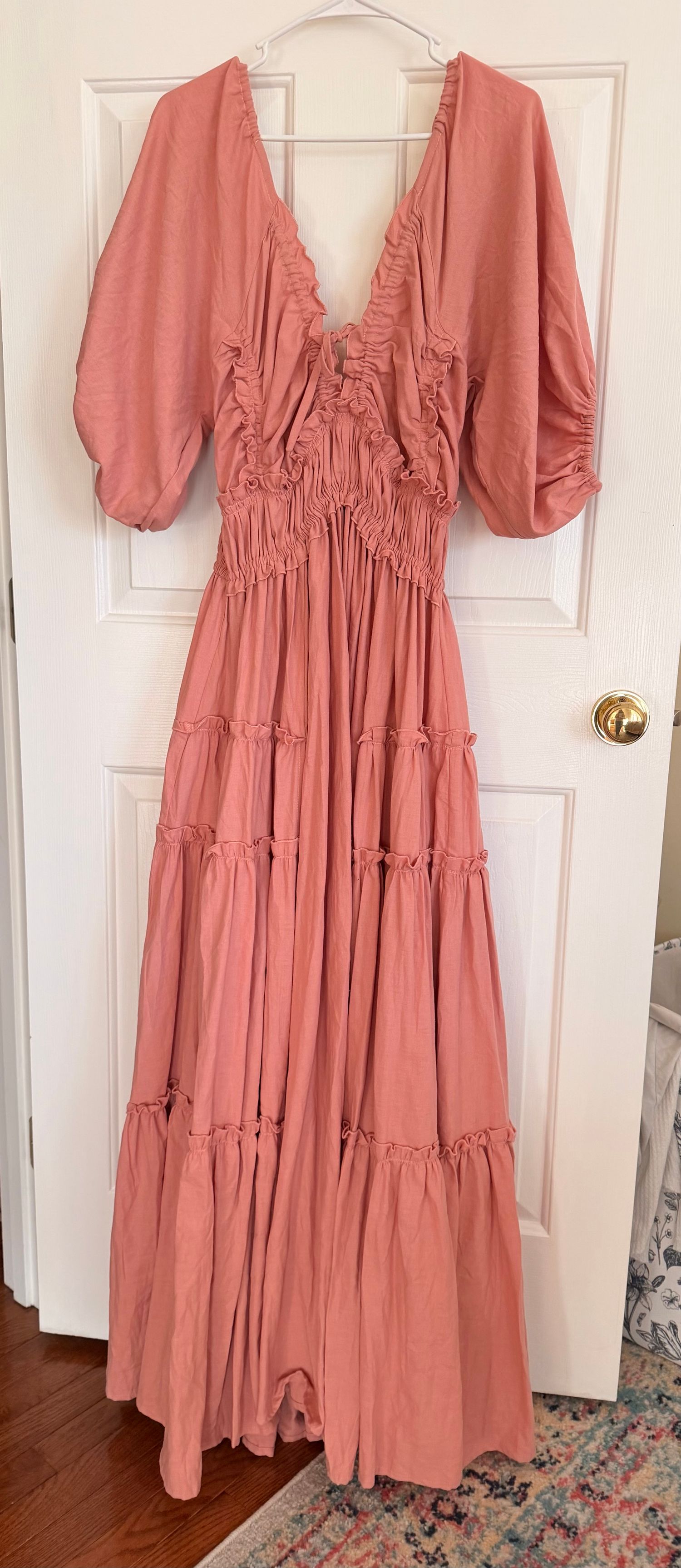 Vintage-style maxi dress in salmon pink with ruched bodice, puff sleeves, and tiered ruffle skirt hanging on white door.
