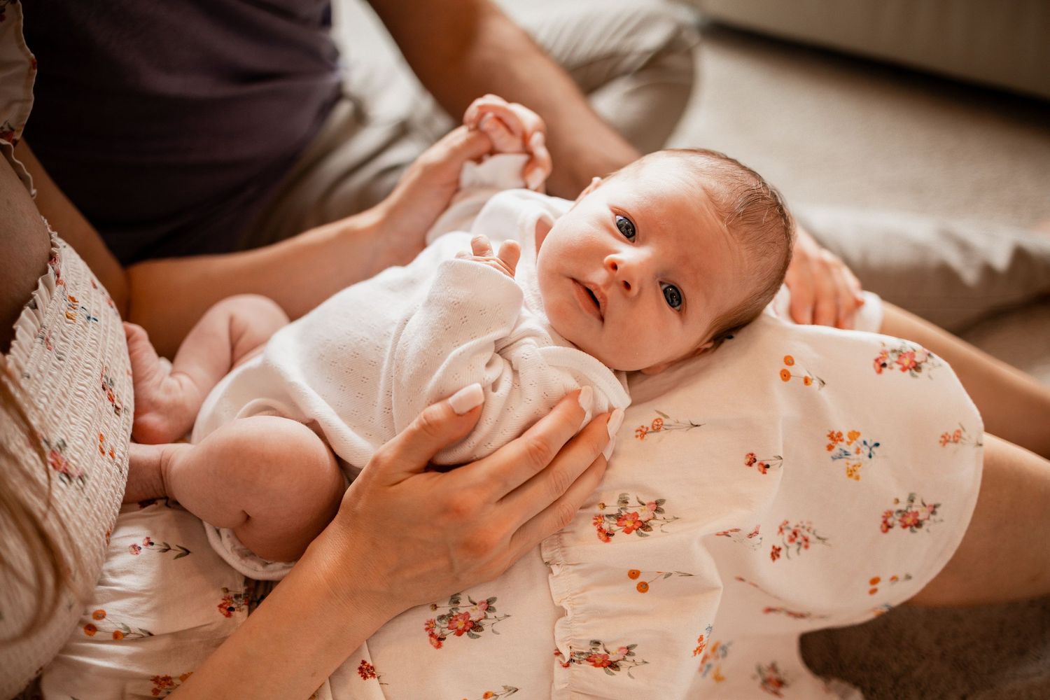 Close-up shot of gentle hands holding a baby wrapped in a floral patterned blanket.