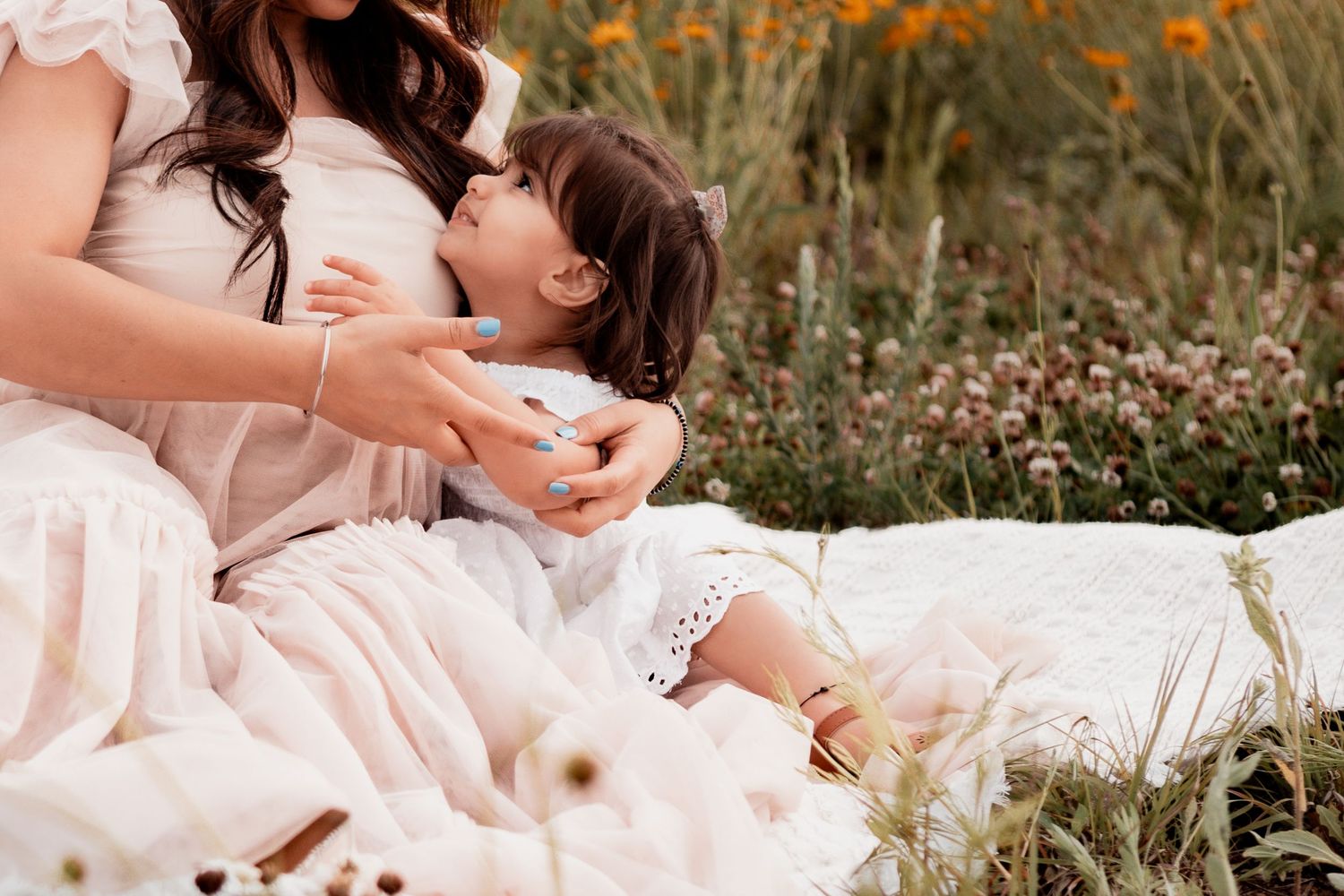 People lounging in white outfits and embracing on grass in golden sunlight during an outdoor photoshoot.