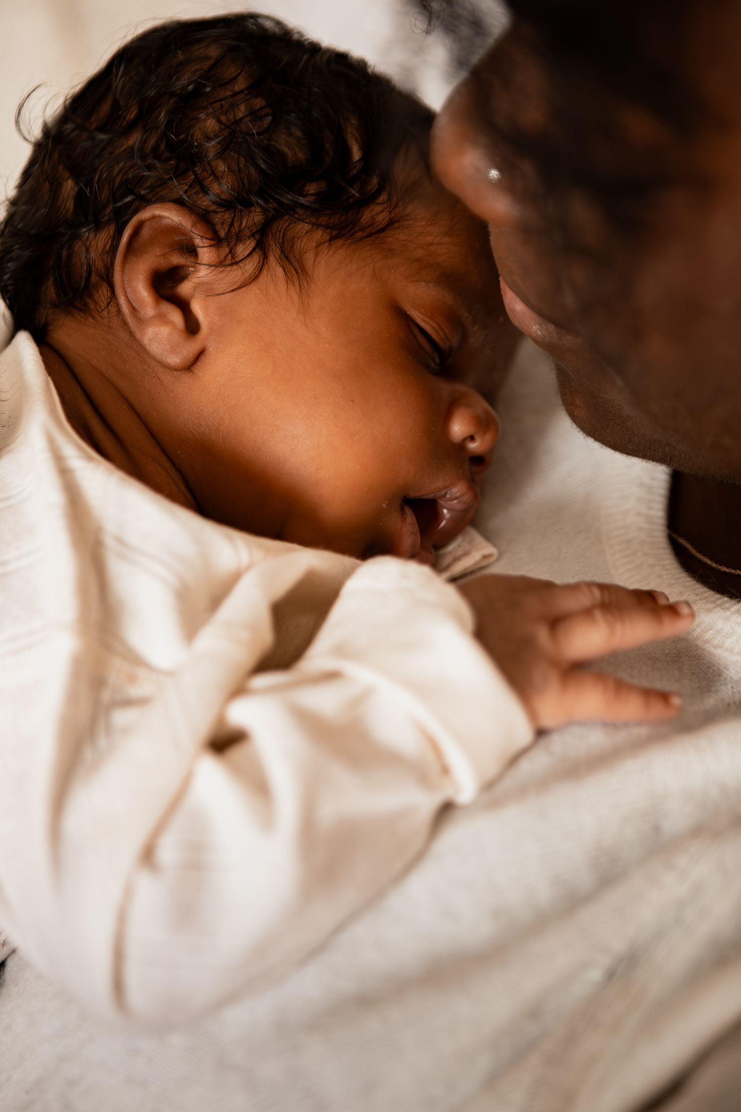 Close-up view of a sleeping baby wrapped in white bedding with soft focus and warm lighting.