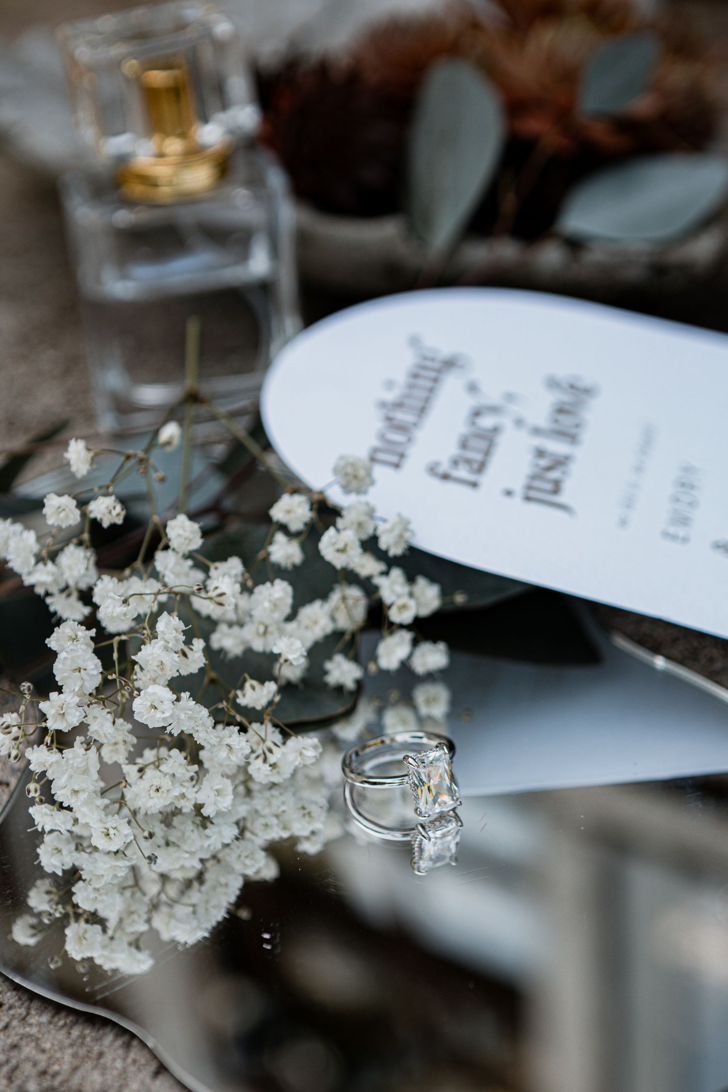 A delicate arrangement of baby's breath flowers next to an engagement ring and perfume bottle with wedding program details.