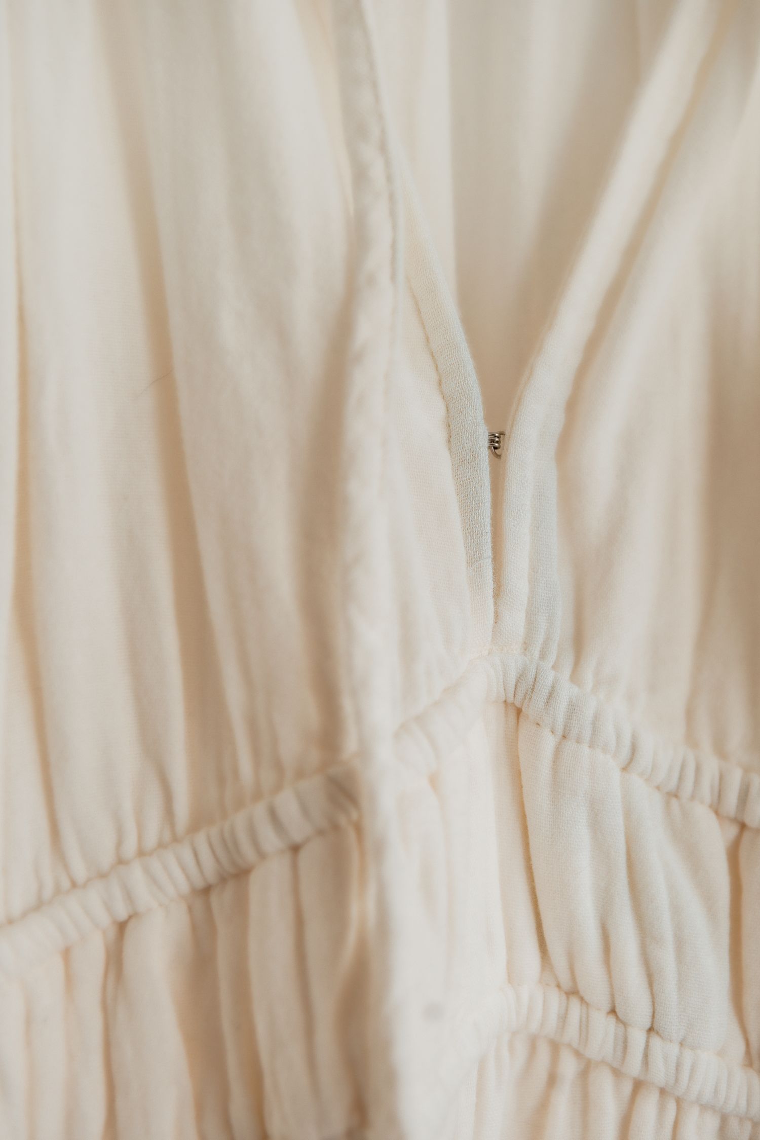 Close-up detail of cream colored gathered fabric with elastic ruching and zipper detail on light textile.