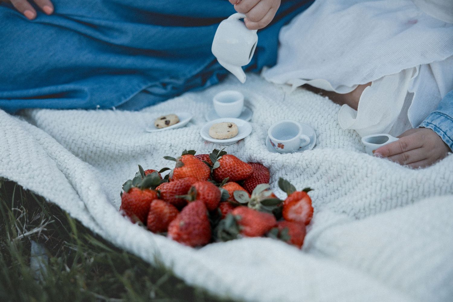Romantic picnic on white blanket with fresh strawberries and coffee cups, outdoor summer setting.