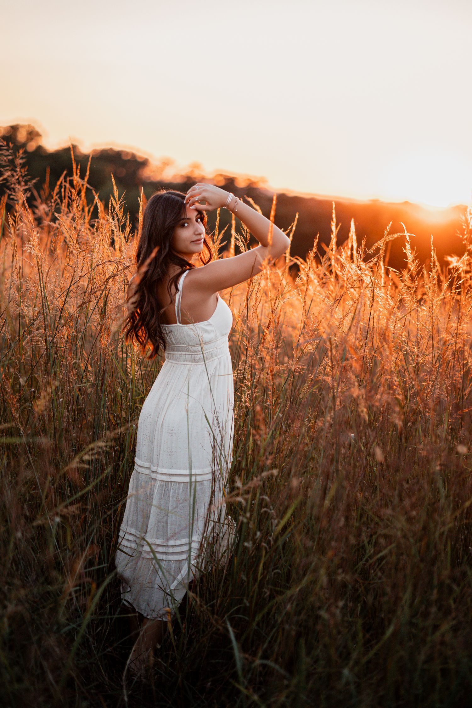 Woman in flowy white dress dances through tall grass field illuminated by golden hour sunlight.
