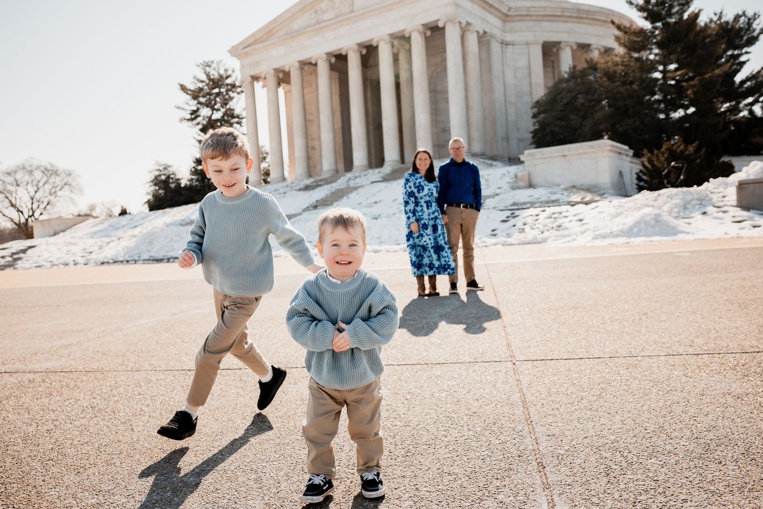 Two young boys run and play outside the Jefferson Memorial in Washington DC on a sunny winter day with their parents nearby.