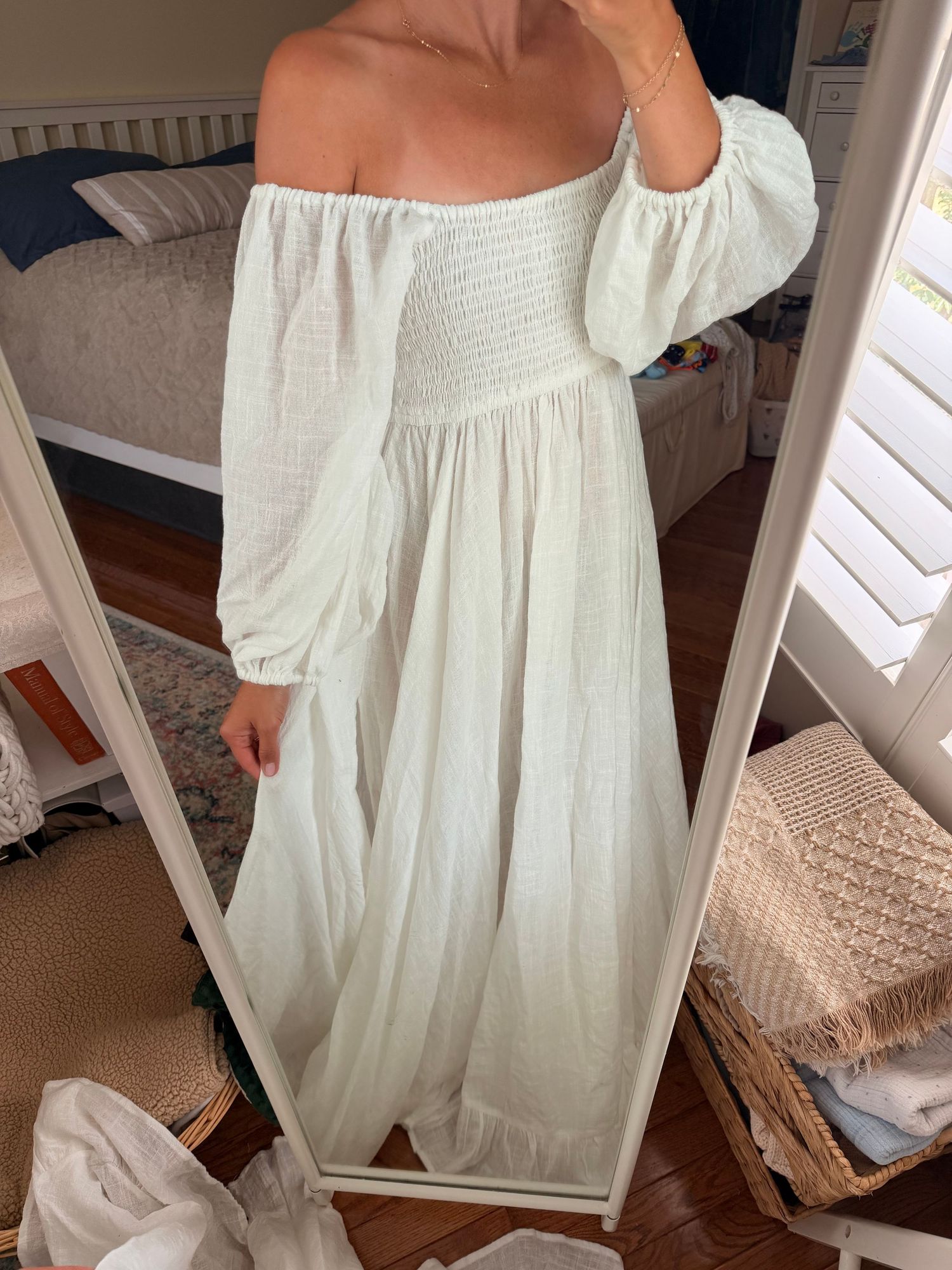 Woman wearing a white off-shoulder smocked bodice maxi dress with billowy sleeves, photographed in mirror.