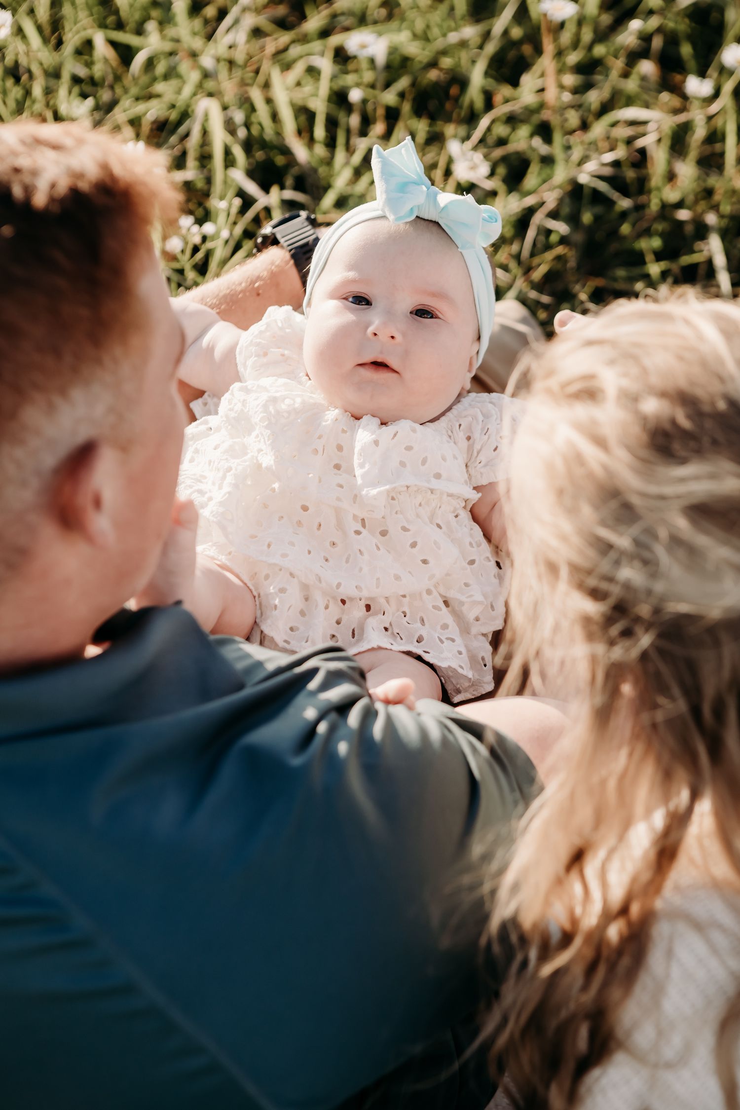 Parents holding their baby dressed in white lace against a natural outdoor background.