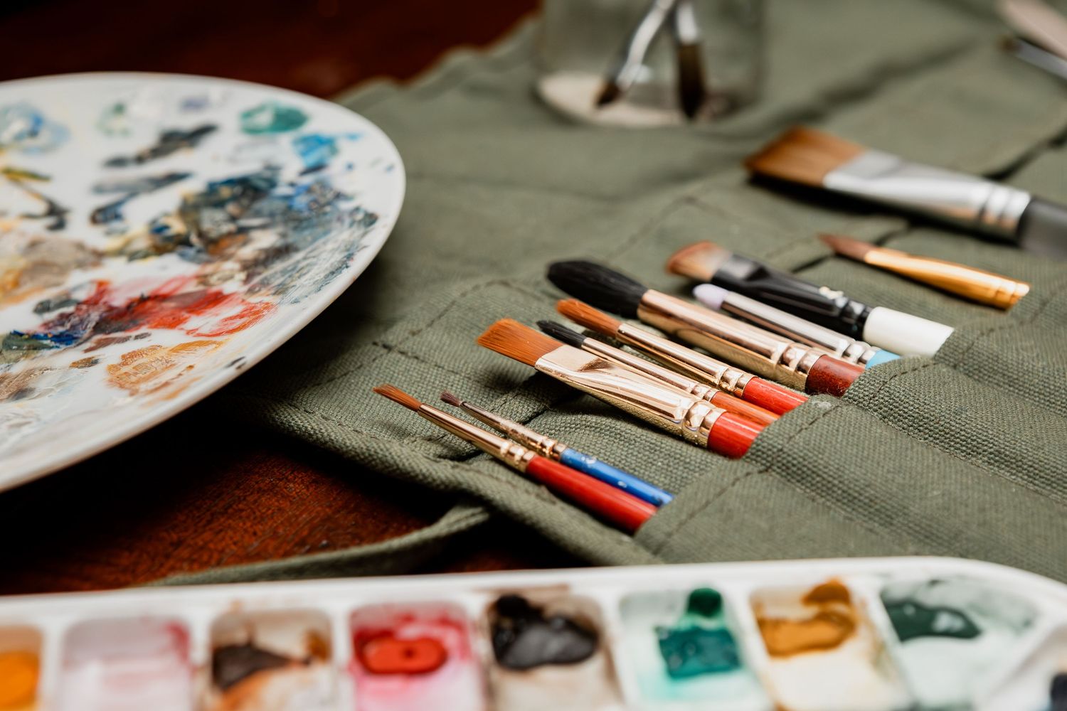 Art supplies including paintbrushes and a paint palette with watercolors laid out on a green surface for painting.