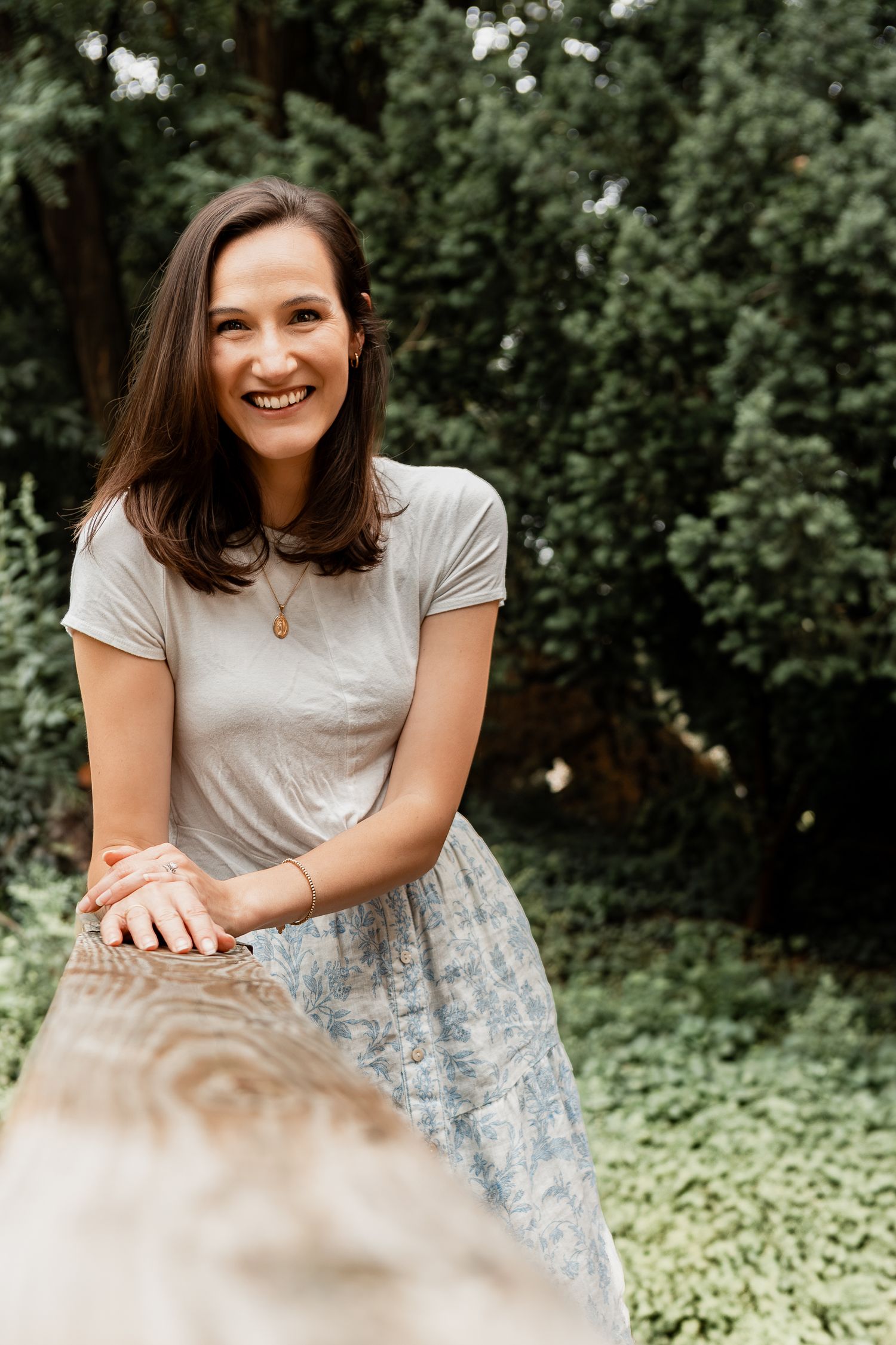 A casual summer portrait outdoors featuring a floral skirt and light colored t-shirt against green foliage.