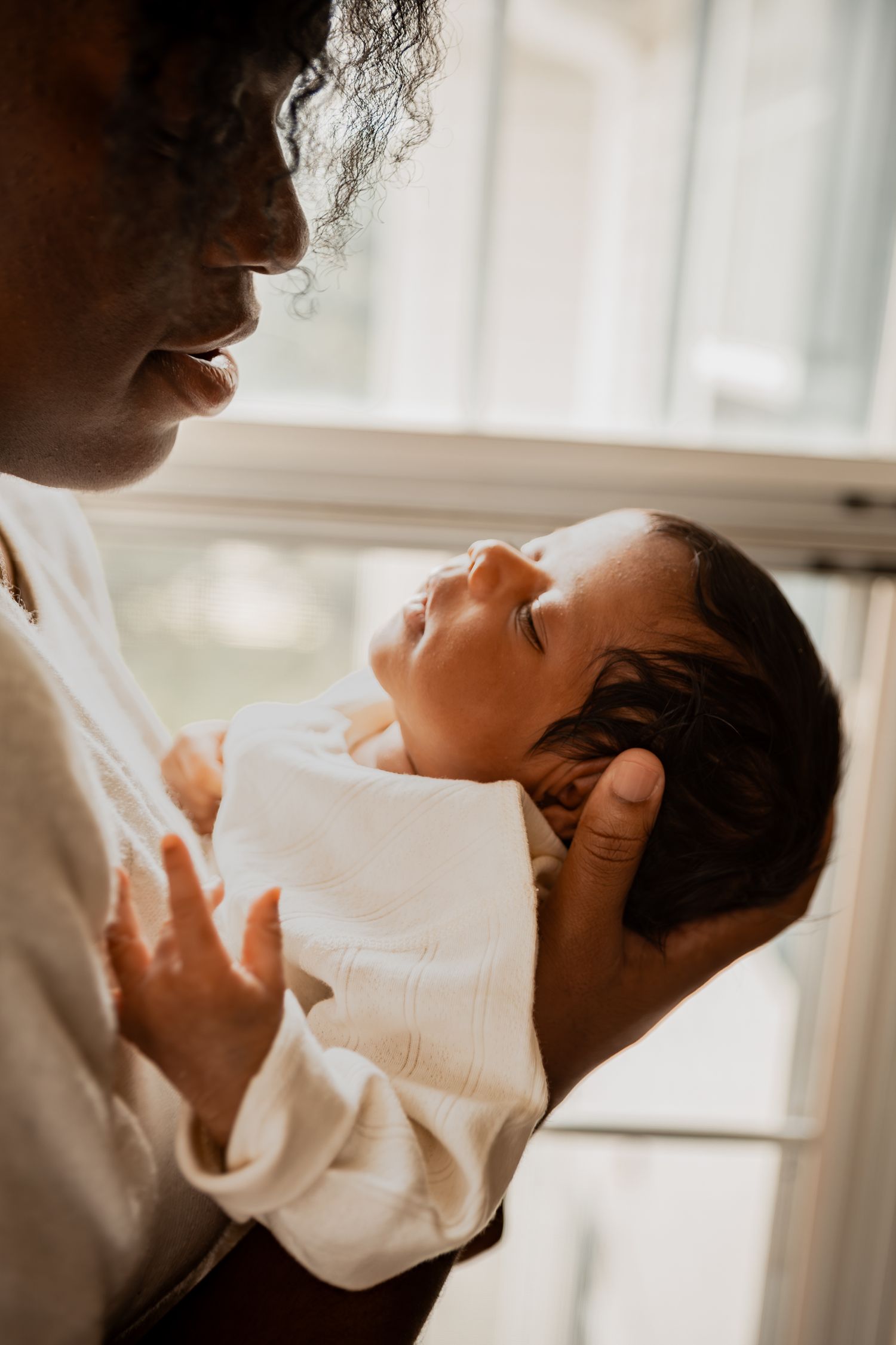 Tender moment captured in warm lighting as person gazes at swaddled newborn baby while holding them close.