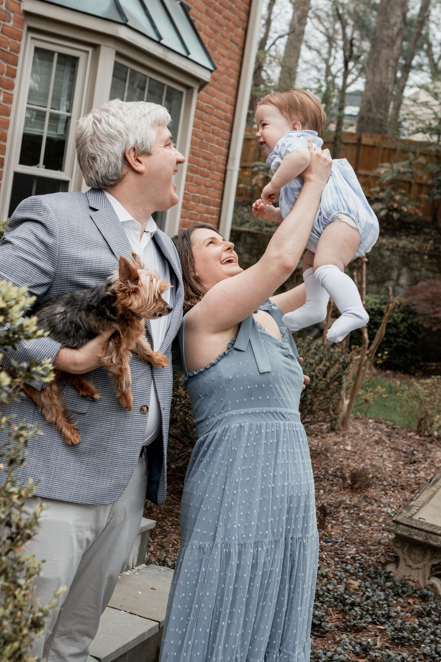 Two people in matching gray and blue outfits laugh together during a candid photoshoot outside a brick building.