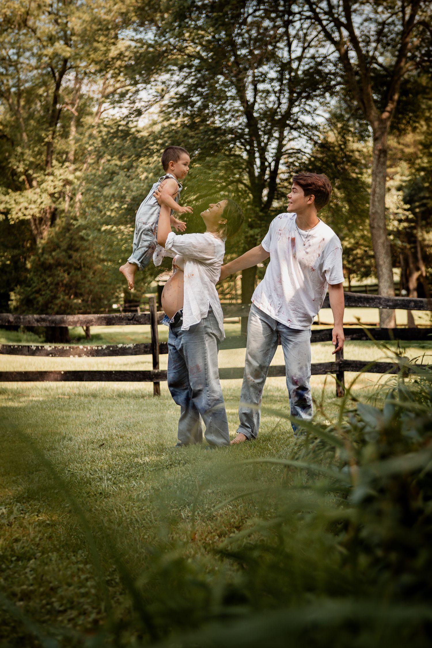 Family playing and running together in a sunny park with trees in the background.