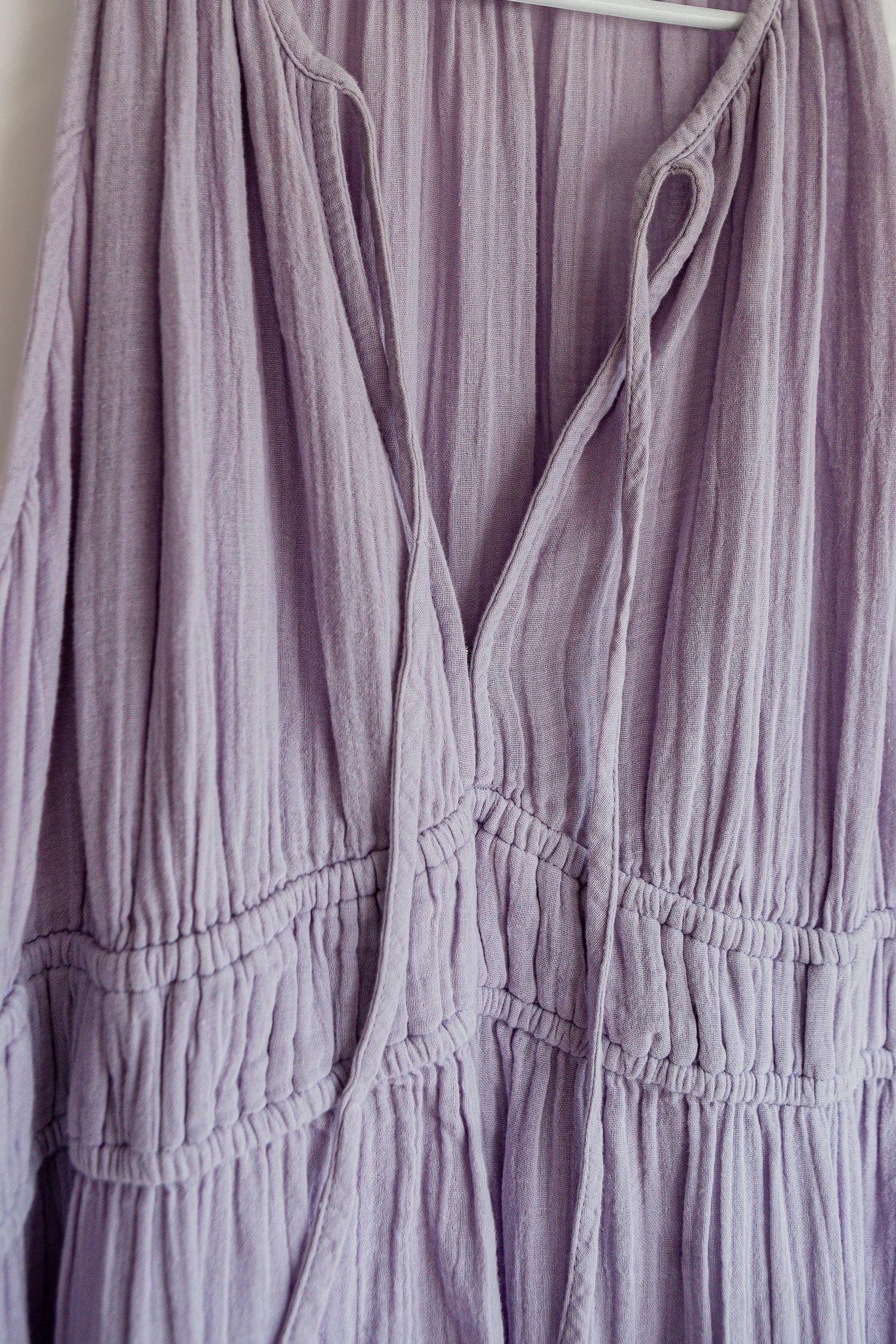 Close-up detail of a lavender cotton dress showing gathered fabric with tiered ruching and a v-neckline opening.