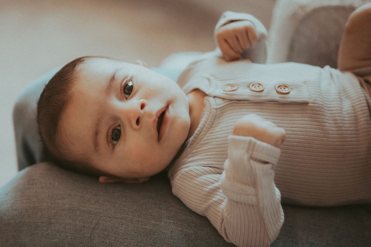 Baby in a beige ribbed onesie lying down during an intimate photoshoot.