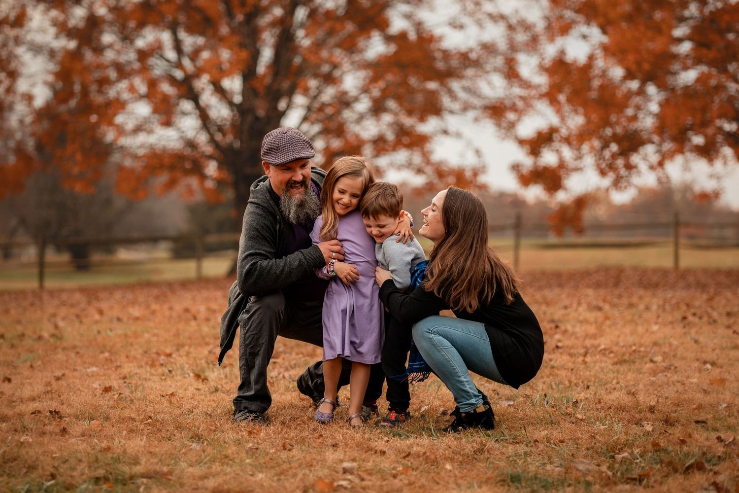 A family sits together on fallen autumn leaves in a park during a warm fall afternoon.