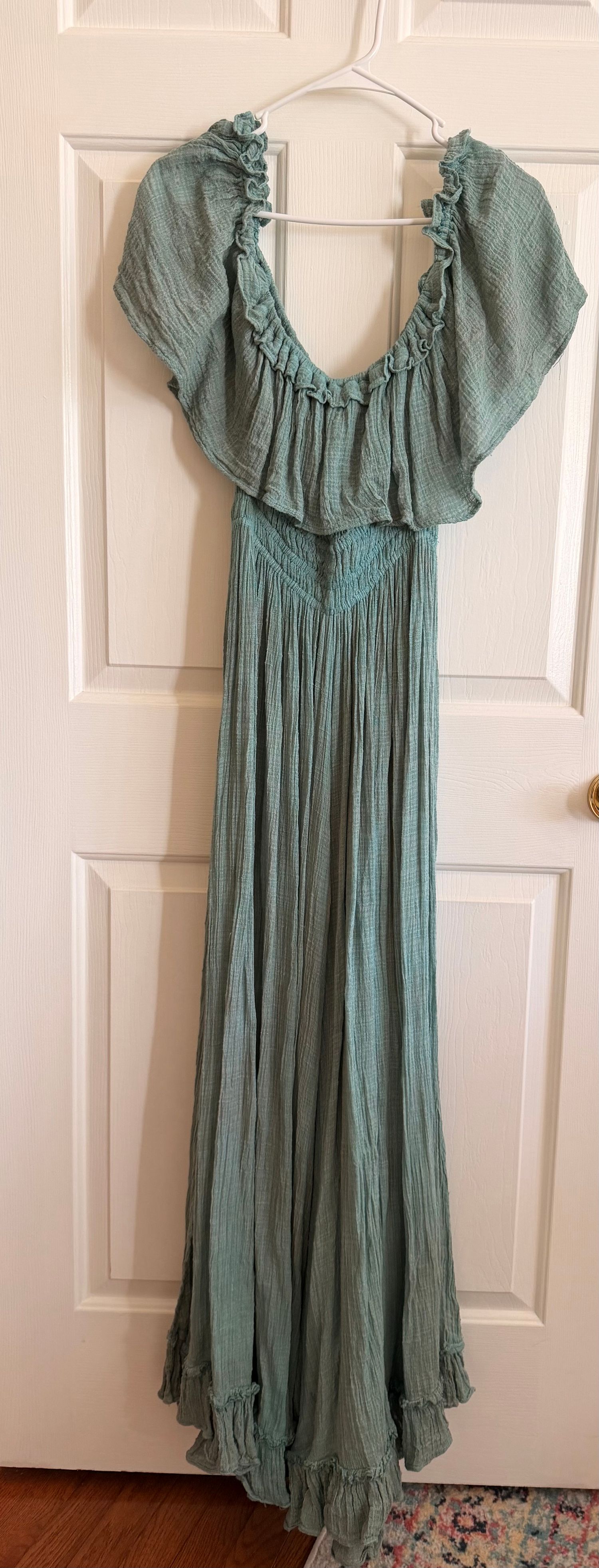 Teal green crinkle gauze maxi dress with ruffled off-shoulder neckline and flutter sleeves, hanging on a white door.
