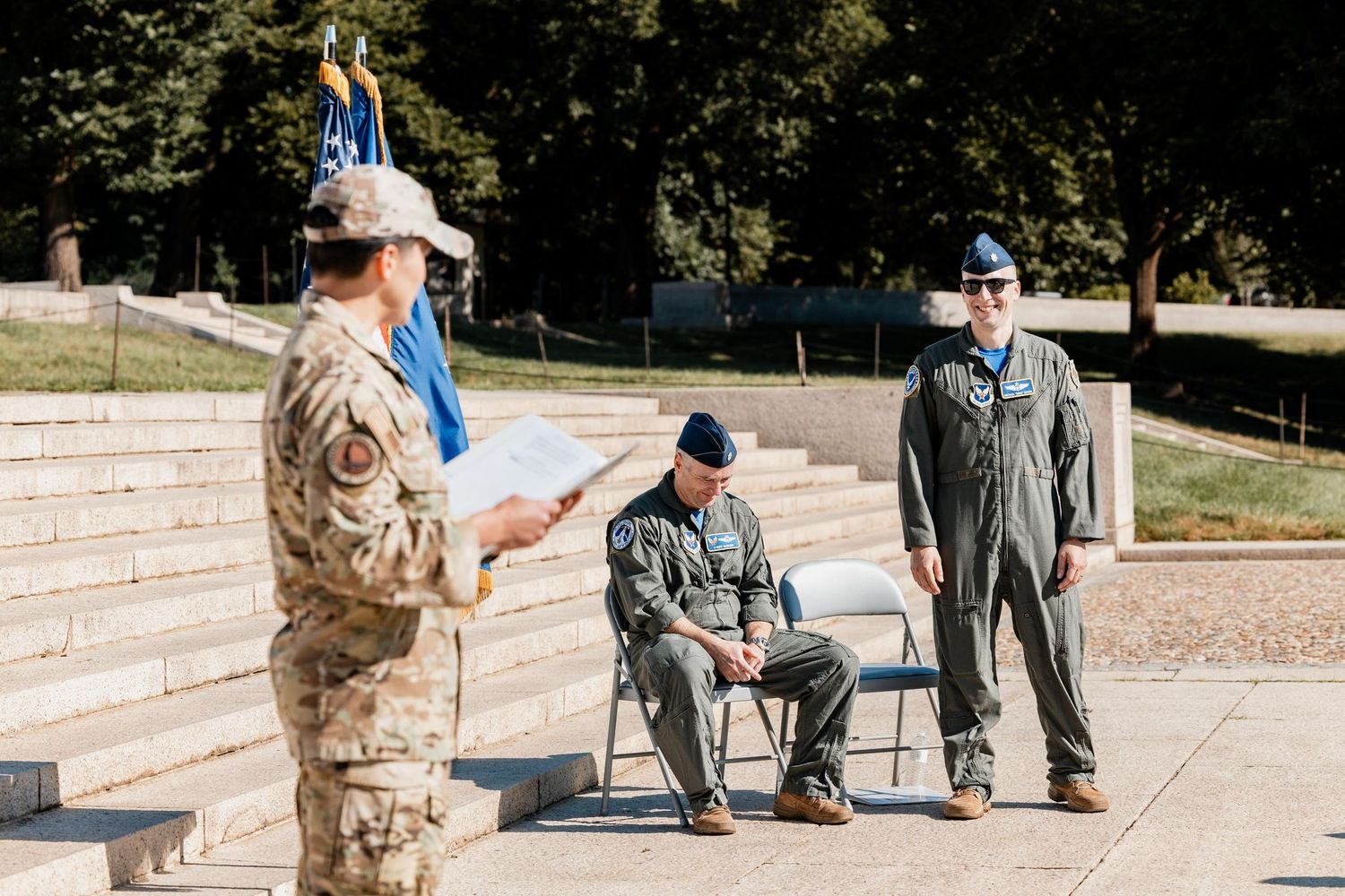 Military personnel in uniform stand outdoors during an official ceremony, with one soldier reading from a document.