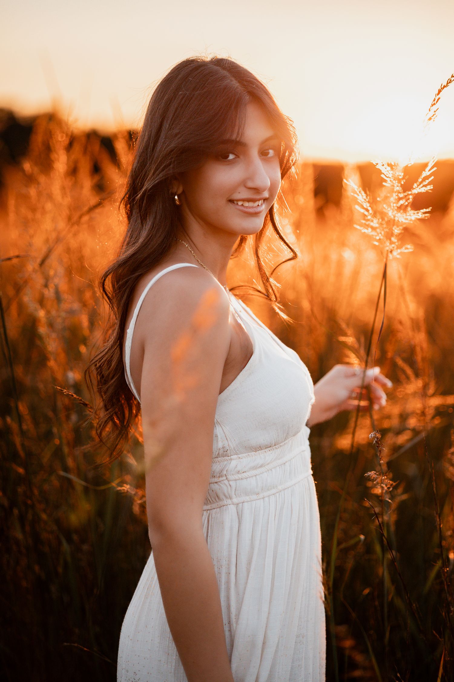 Ethereal sunset portrait in white sundress amid golden grass and glowing light.