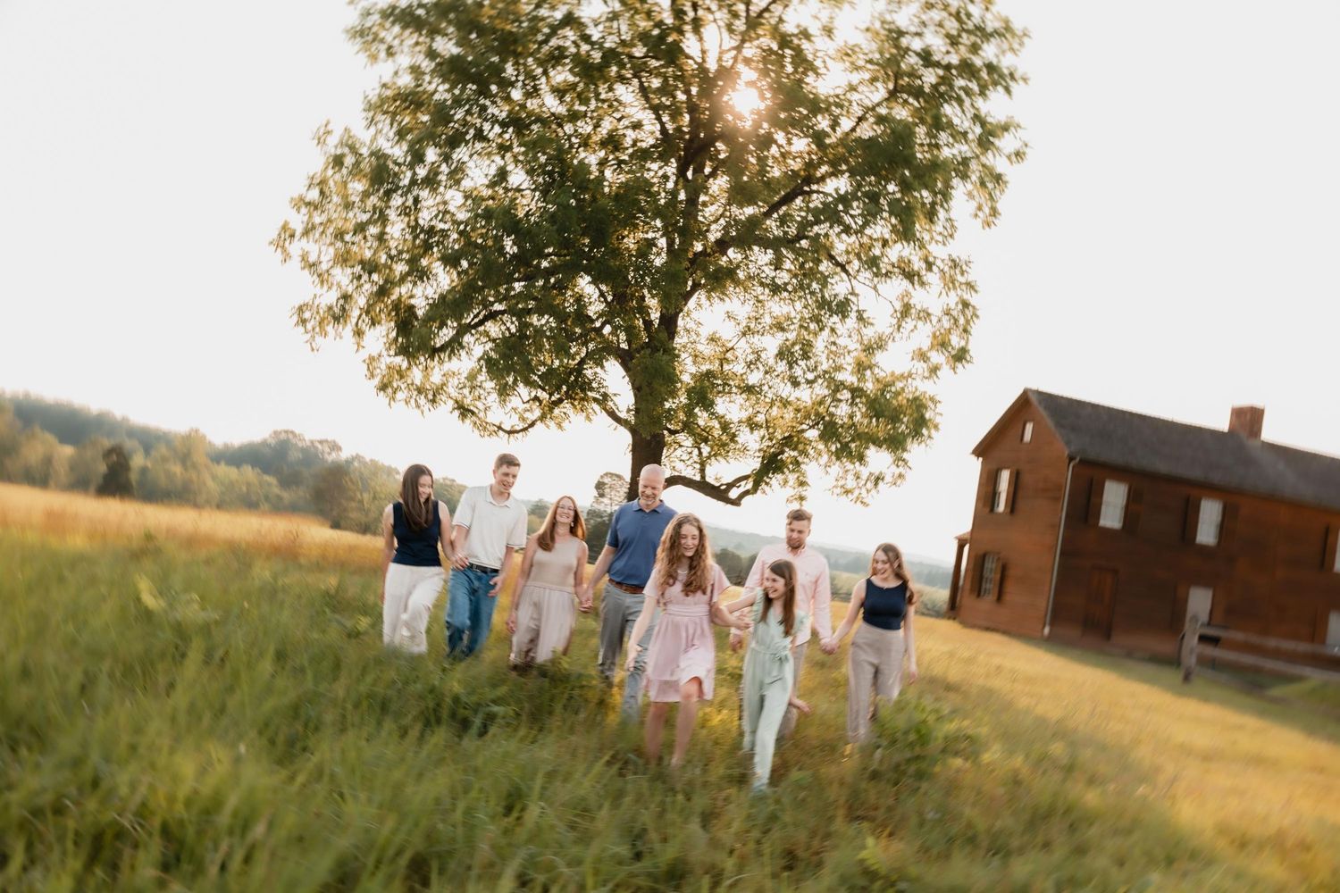 Large family walking through a sunlit meadow with a large tree and historic building in the background.