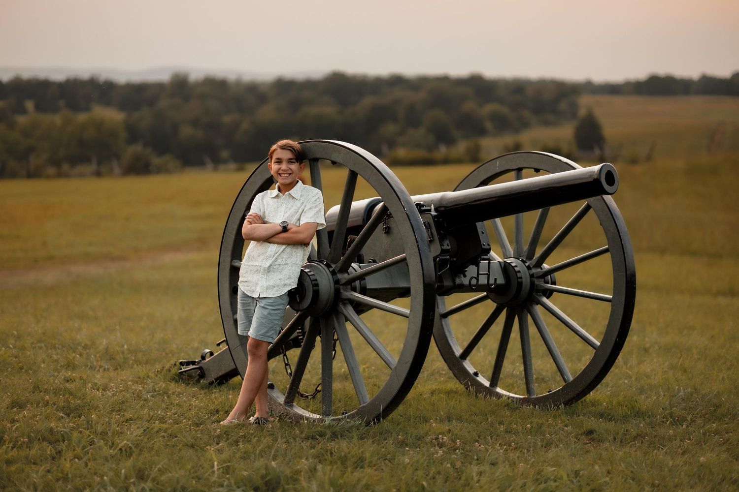 Woman posing beside a historic Civil War cannon on a green battlefield at dusk.