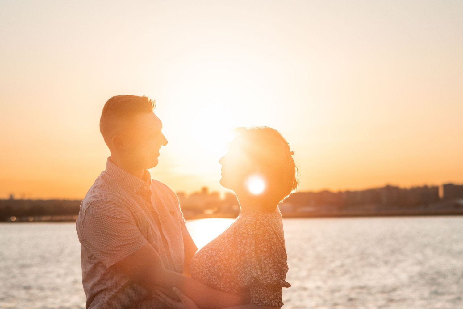 A couple silhouetted against a golden sunset sky over the ocean, creating a romantic backlit scene.
