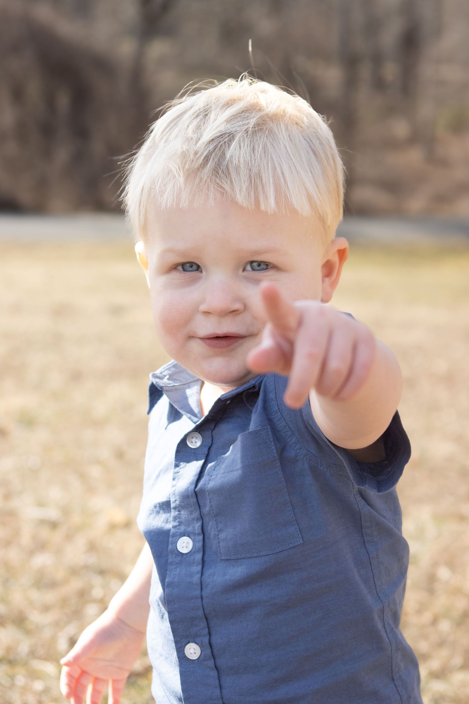 Toddler in blue polo shirt pointing while smiling outdoors.