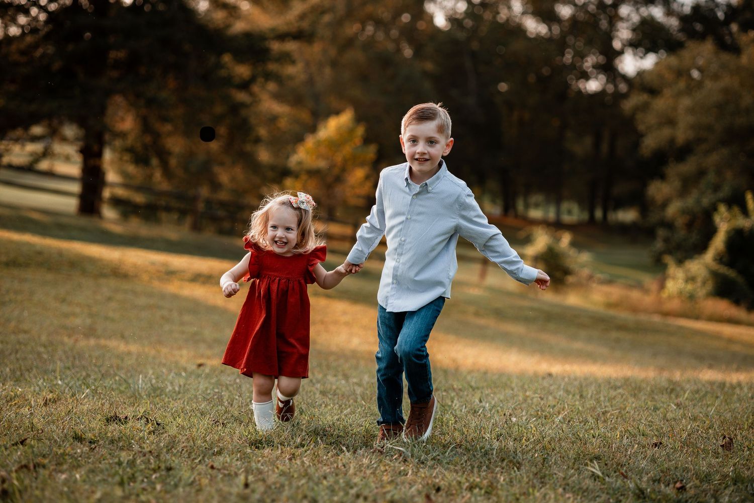 Two young children holding hands and running together on a grassy hill during golden hour.