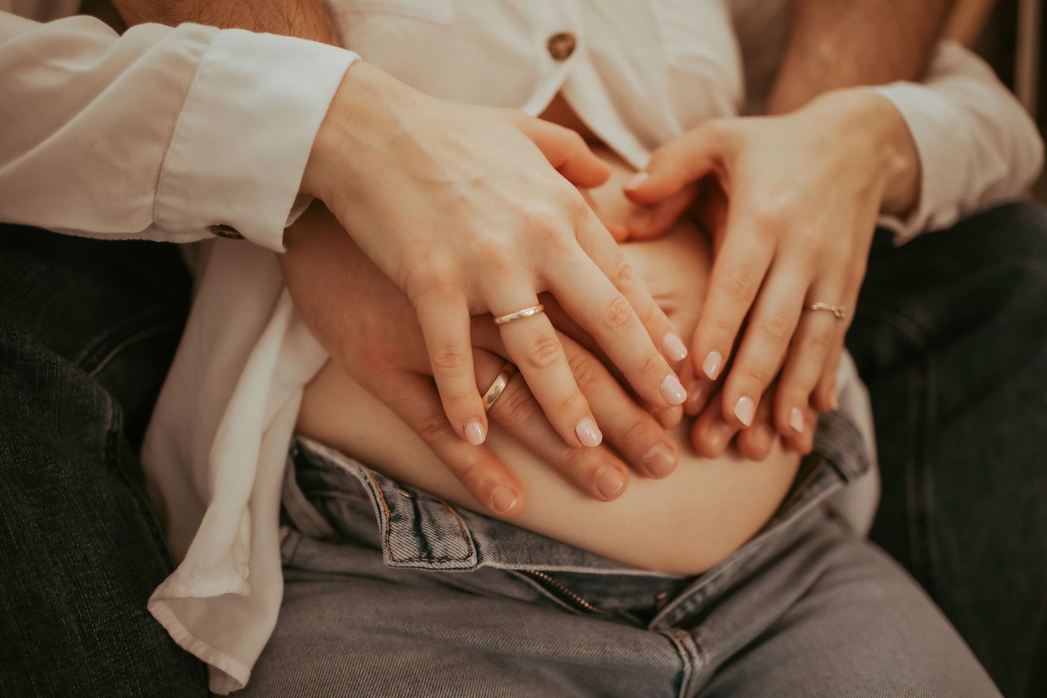 Close-up shot of hands resting on a lap wearing a wedding ring and white shirt.