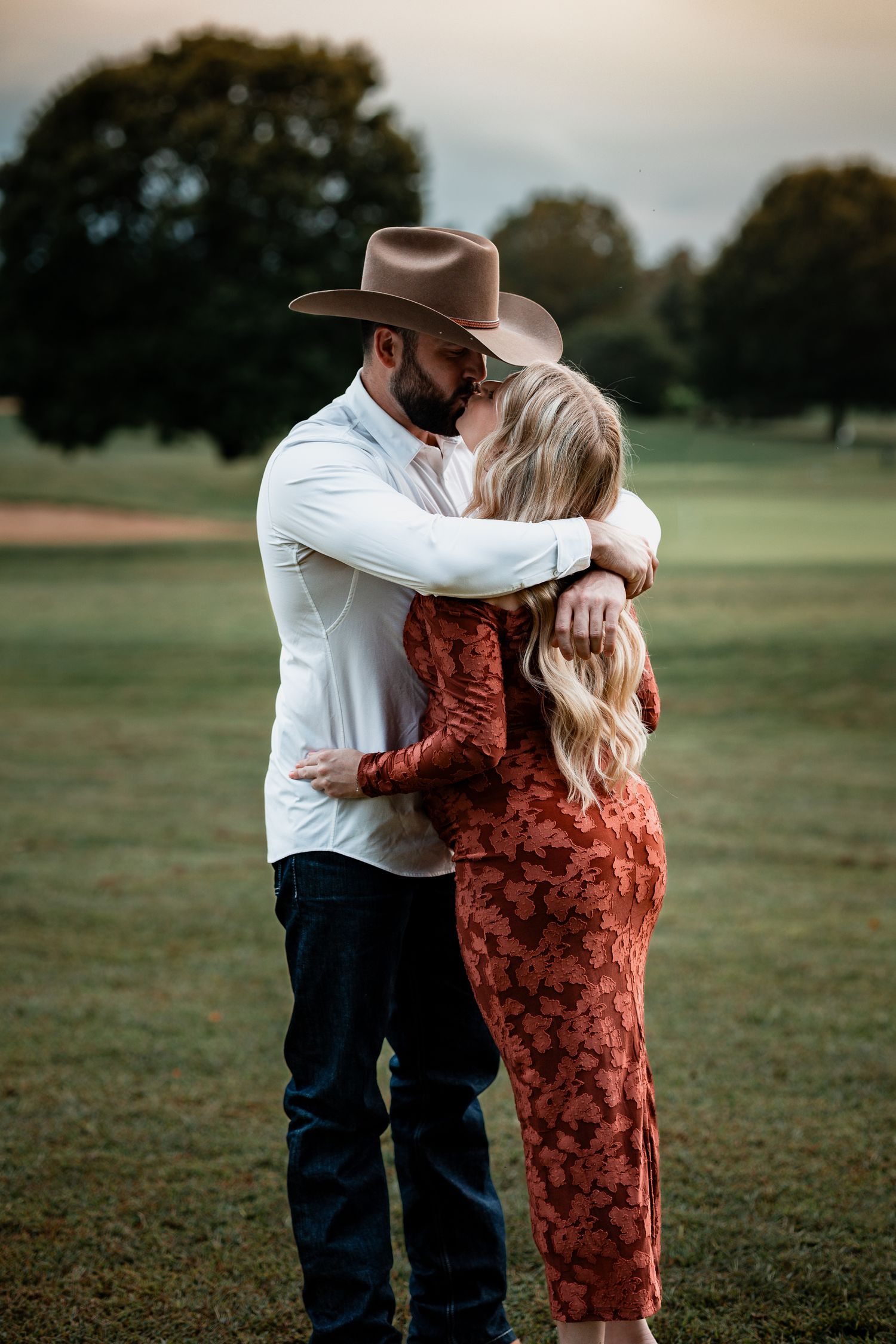 A romantic couple's photo session in a field showing tender moments and embraces at sunset.