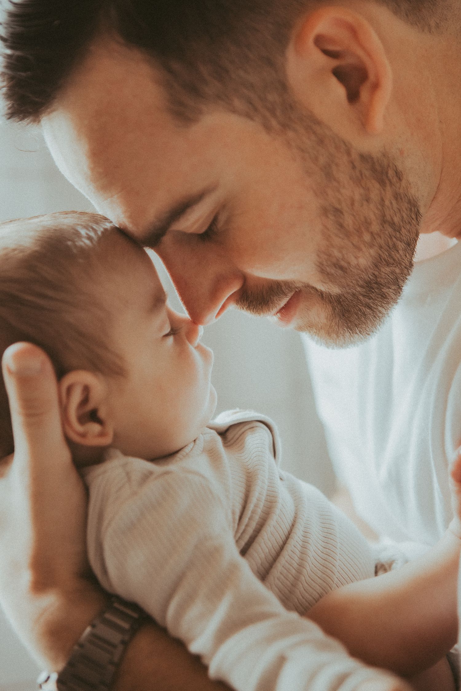 A tender moment captured in warm lighting showing a parent gently embracing and kissing a baby in white clothing.
