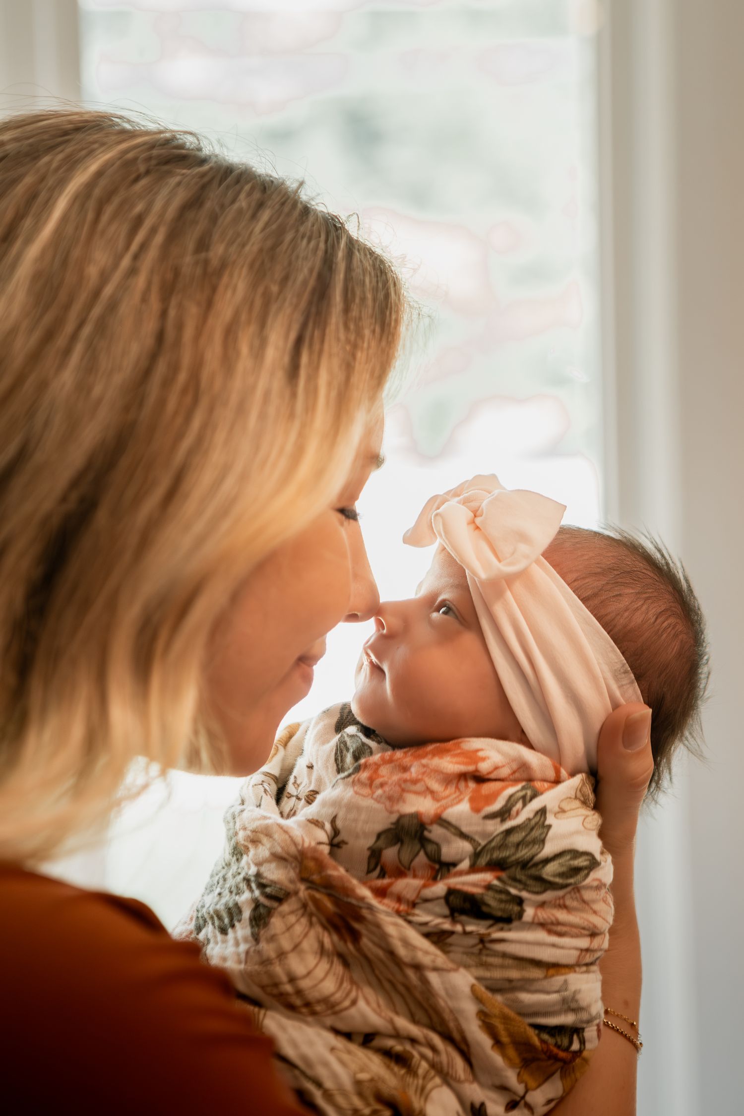 A tender moment shows someone cradling and lovingly kissing a swaddled newborn baby wrapped in a floral blanket.