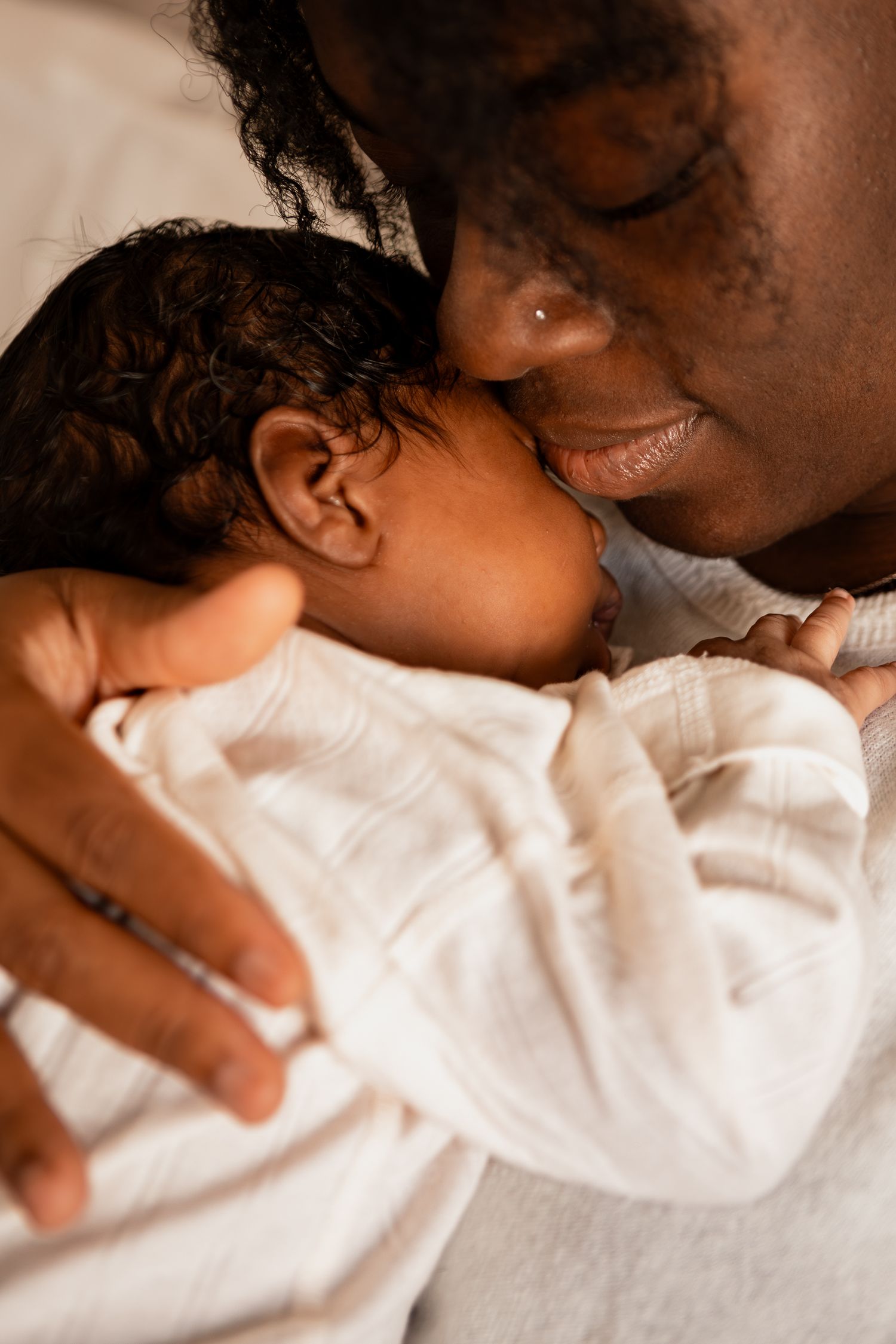 A tender moment between parent and baby in white clothing is captured in warm lighting.
