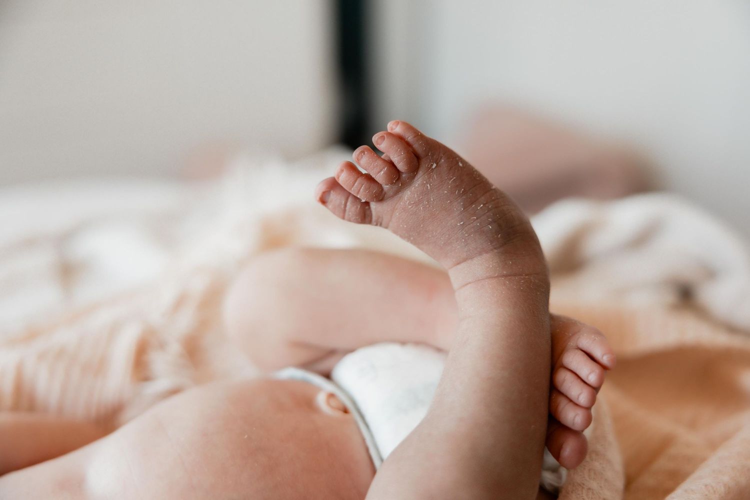 Close-up of a newborn baby's tiny feet and hands resting on a soft peach blanket.