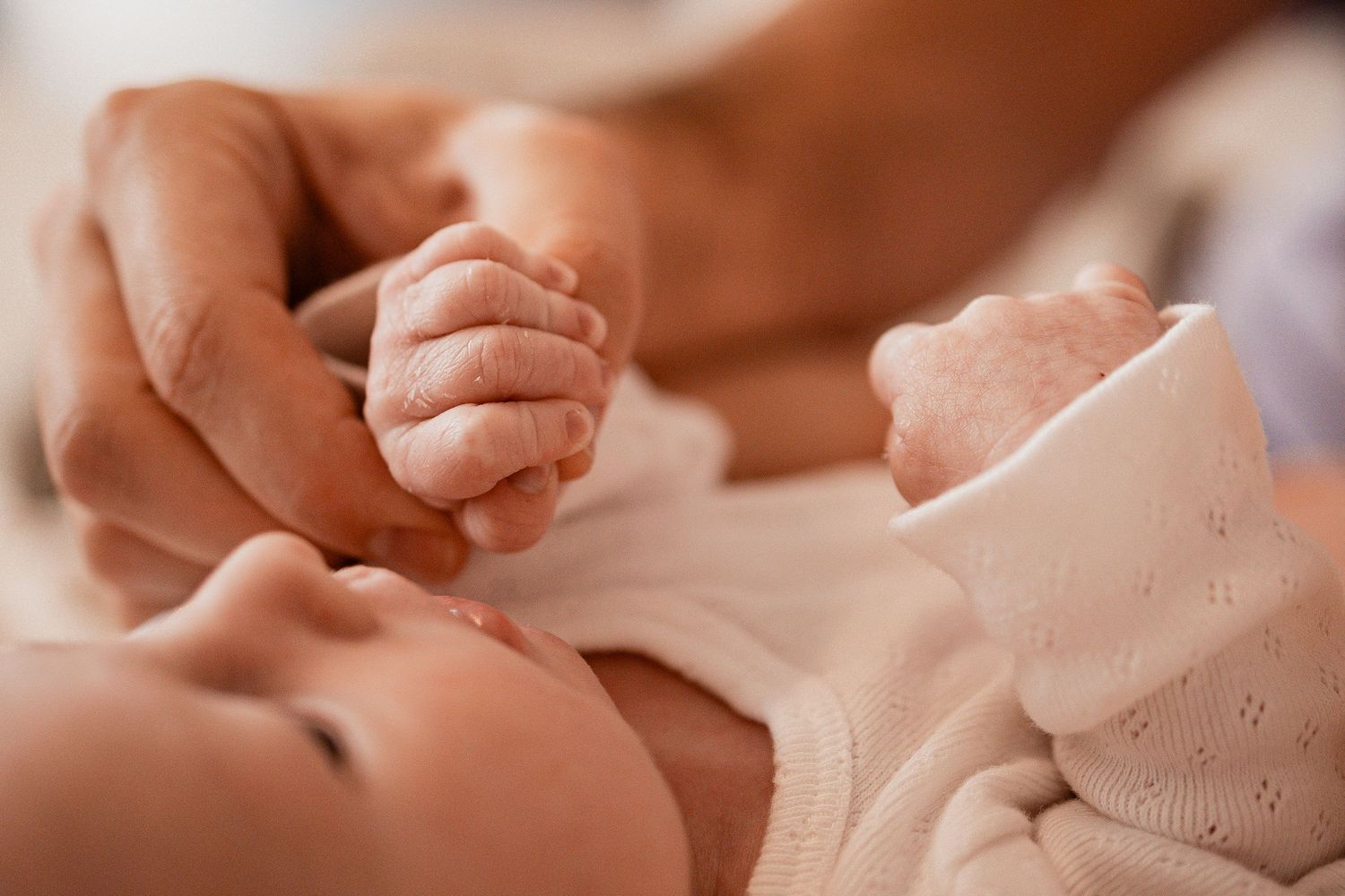 Close-up of baby's tiny hands being gently held by adult hands in warm lighting.