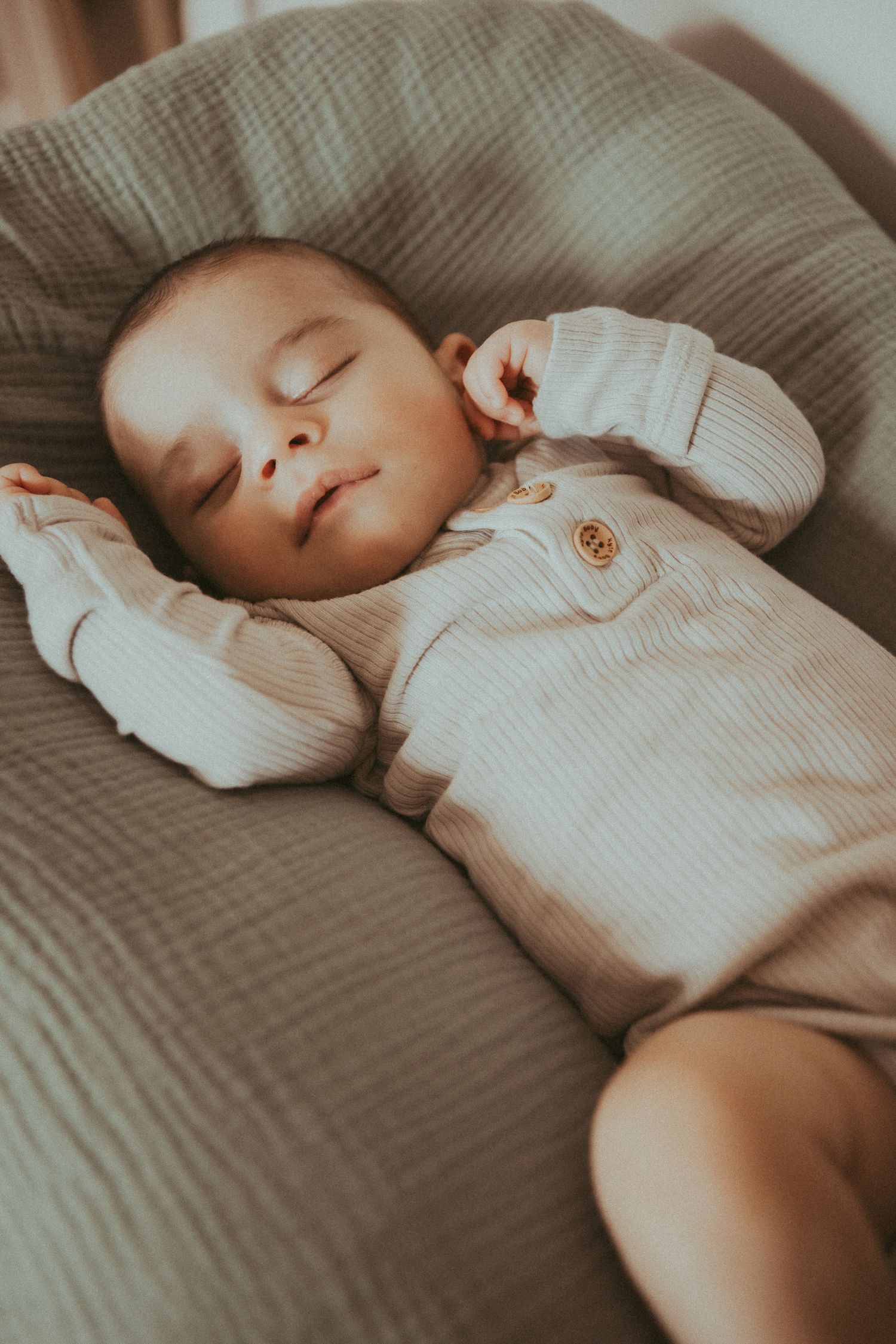 Sleeping baby in white ribbed onesie resting peacefully on gray bedding.