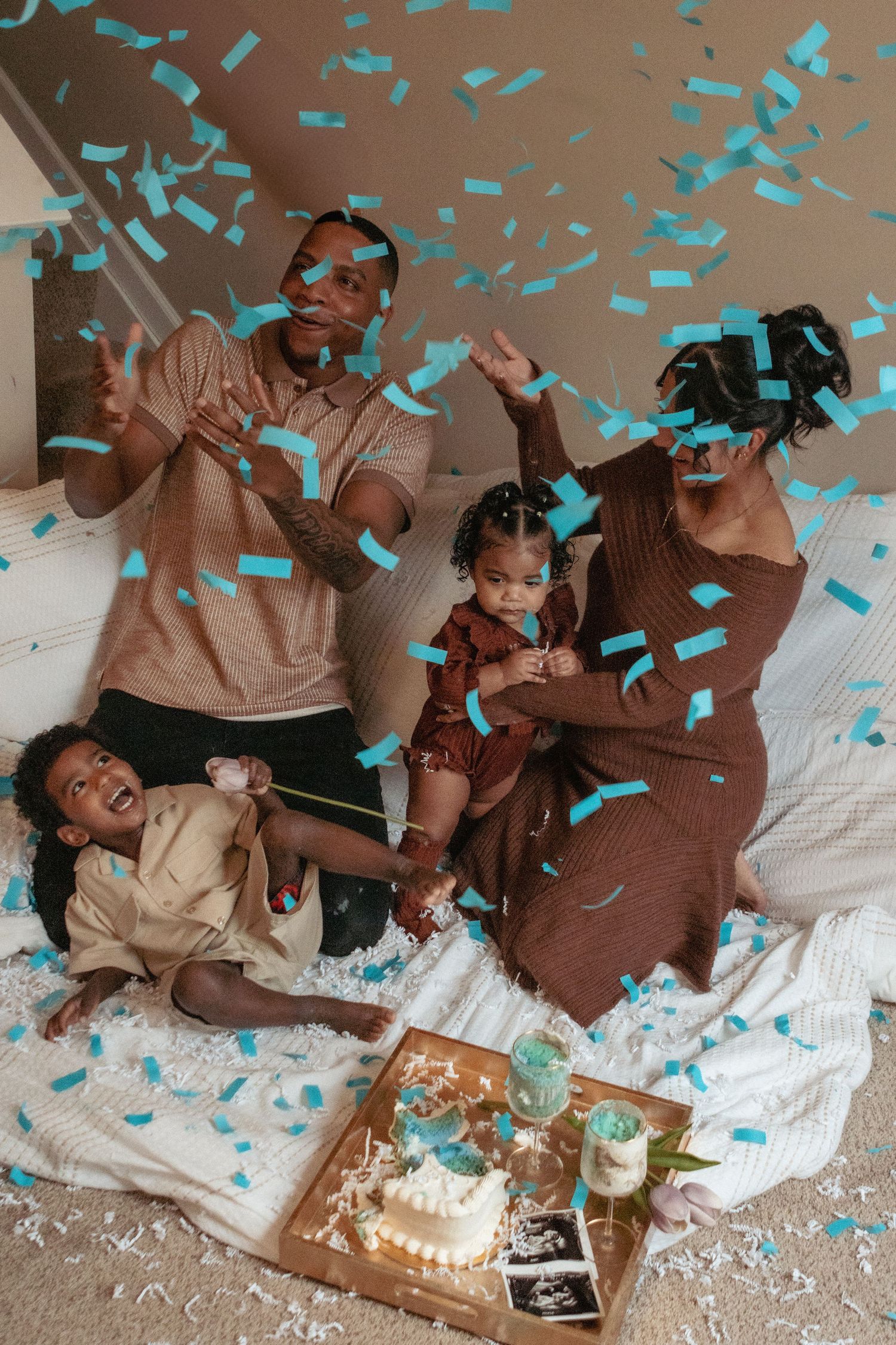 A joyful gender reveal celebration with confetti throwing, ultrasound photo, and blue confetti indicating it's a boy.