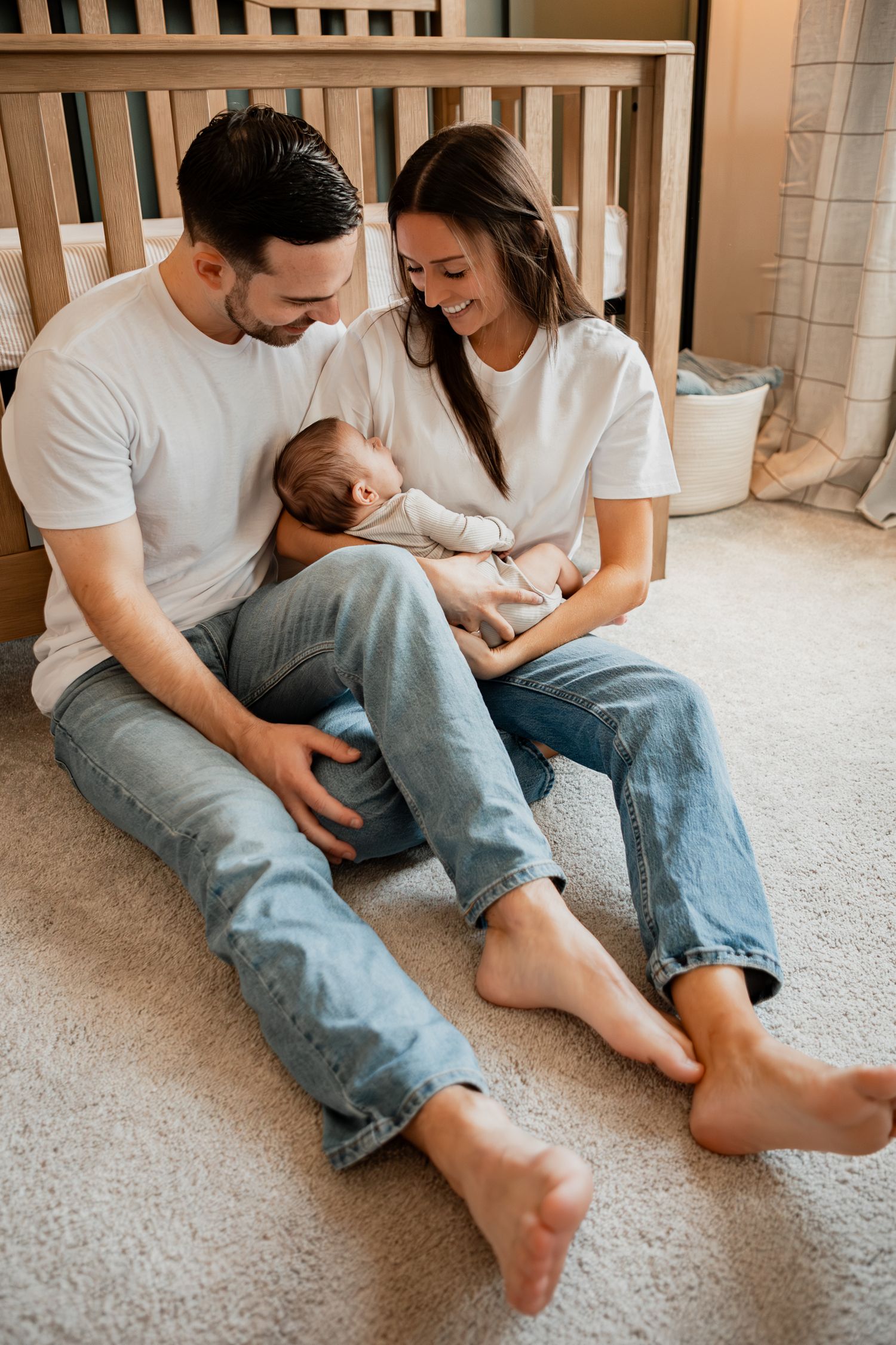 Couple in casual white shirts and jeans sit intimately on carpet floor sharing playful moments together.