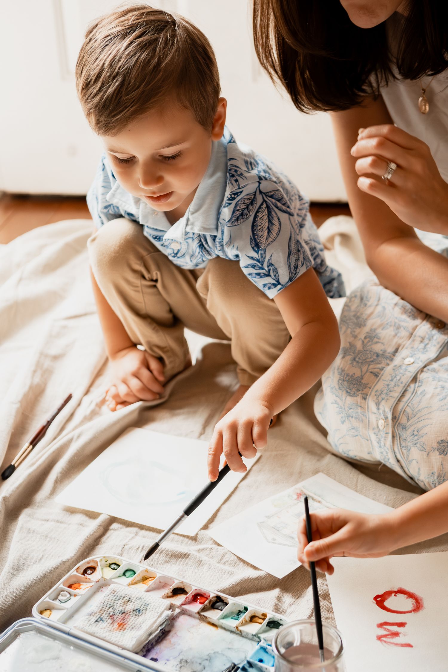 Child in blue floral shirt focuses intently while painting or drawing on paper with brush in series of connected images.