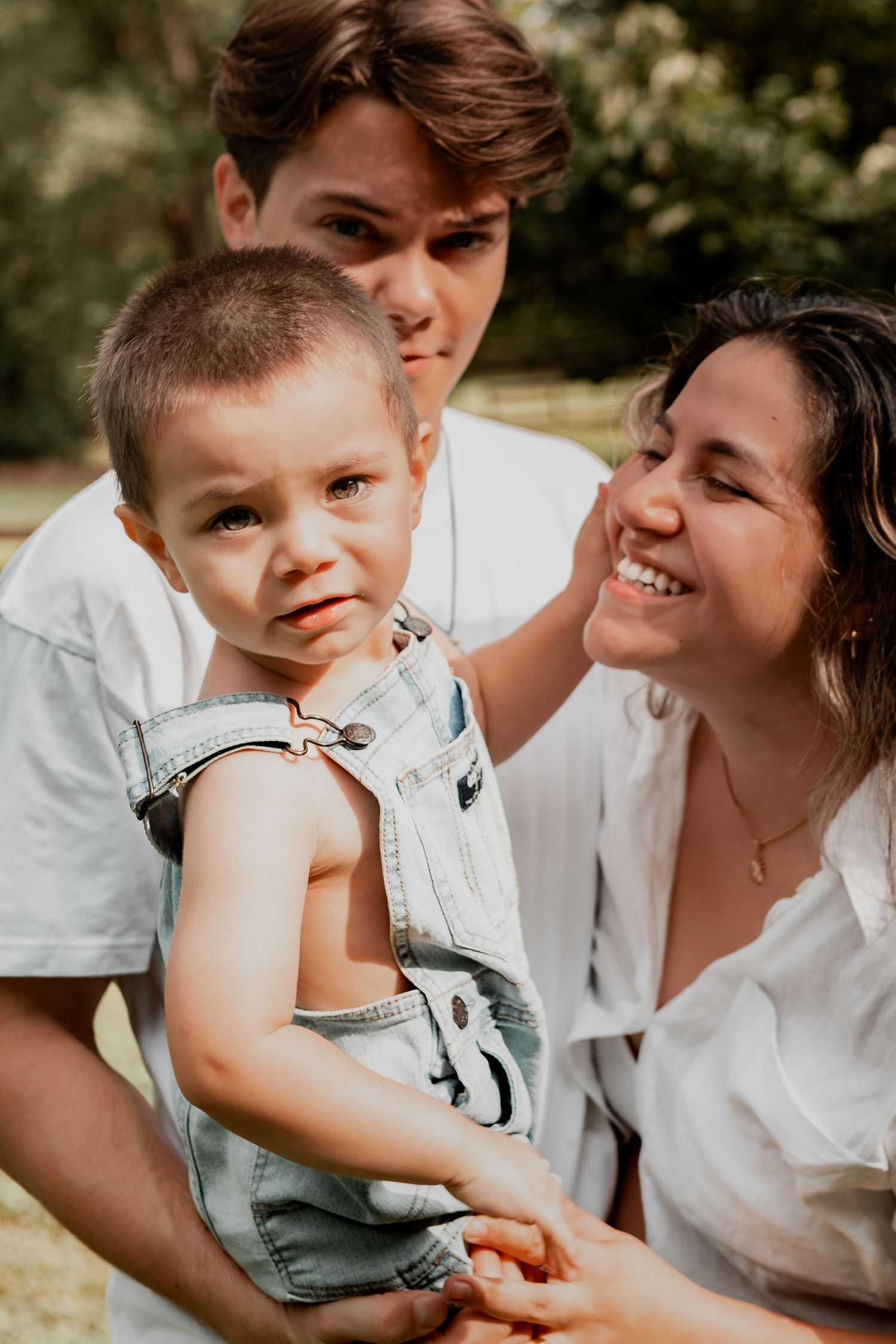 A young family shares a candid outdoor moment together, dressed in white and looking joyful in natural lighting.