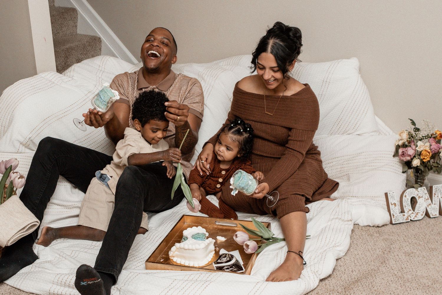 A family shares a joyful moment together while having a cozy breakfast picnic on bed with white linens.