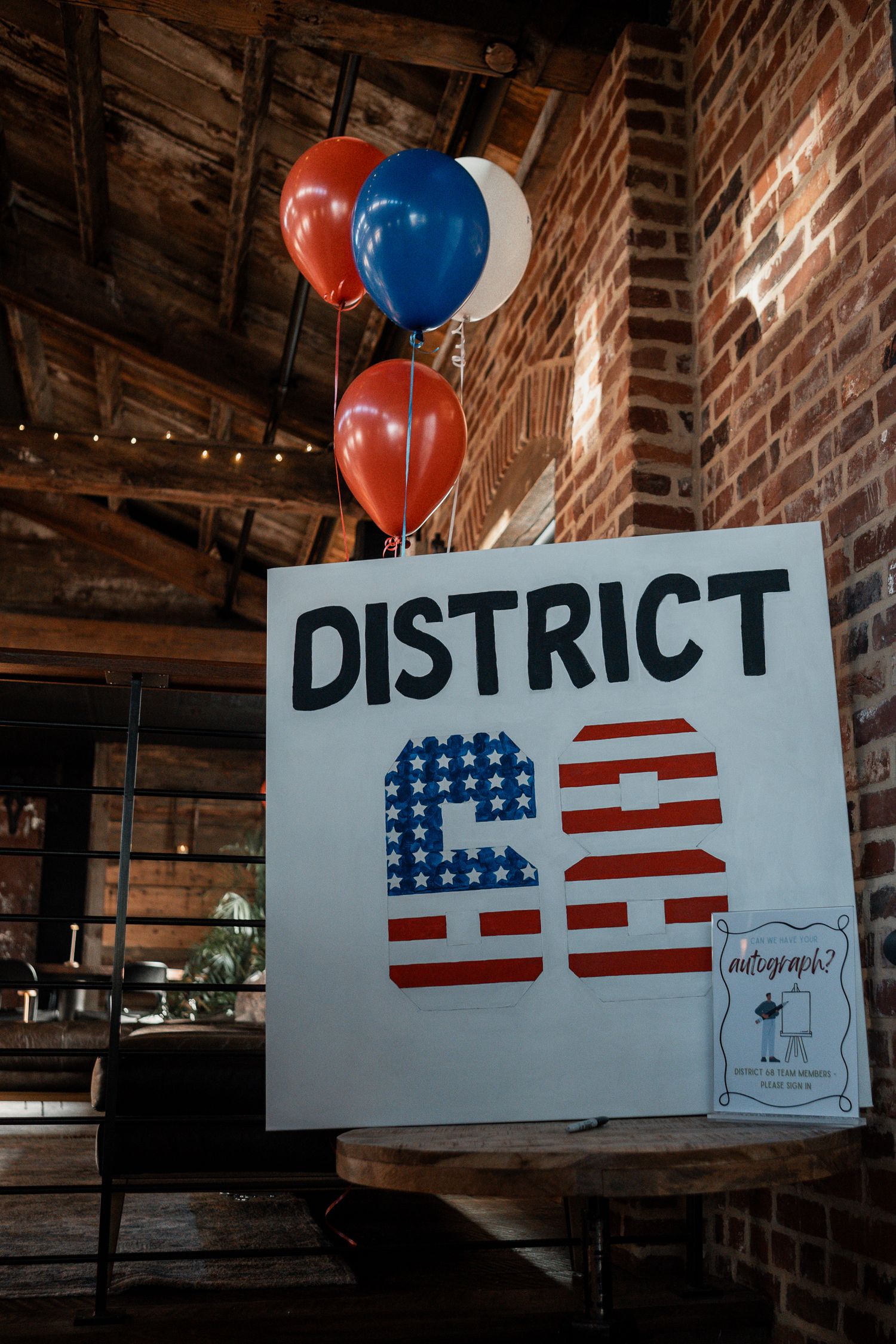 A patriotic sign reading 'District 53' decorated with American flag colors and red and blue balloons in a rustic venue.
