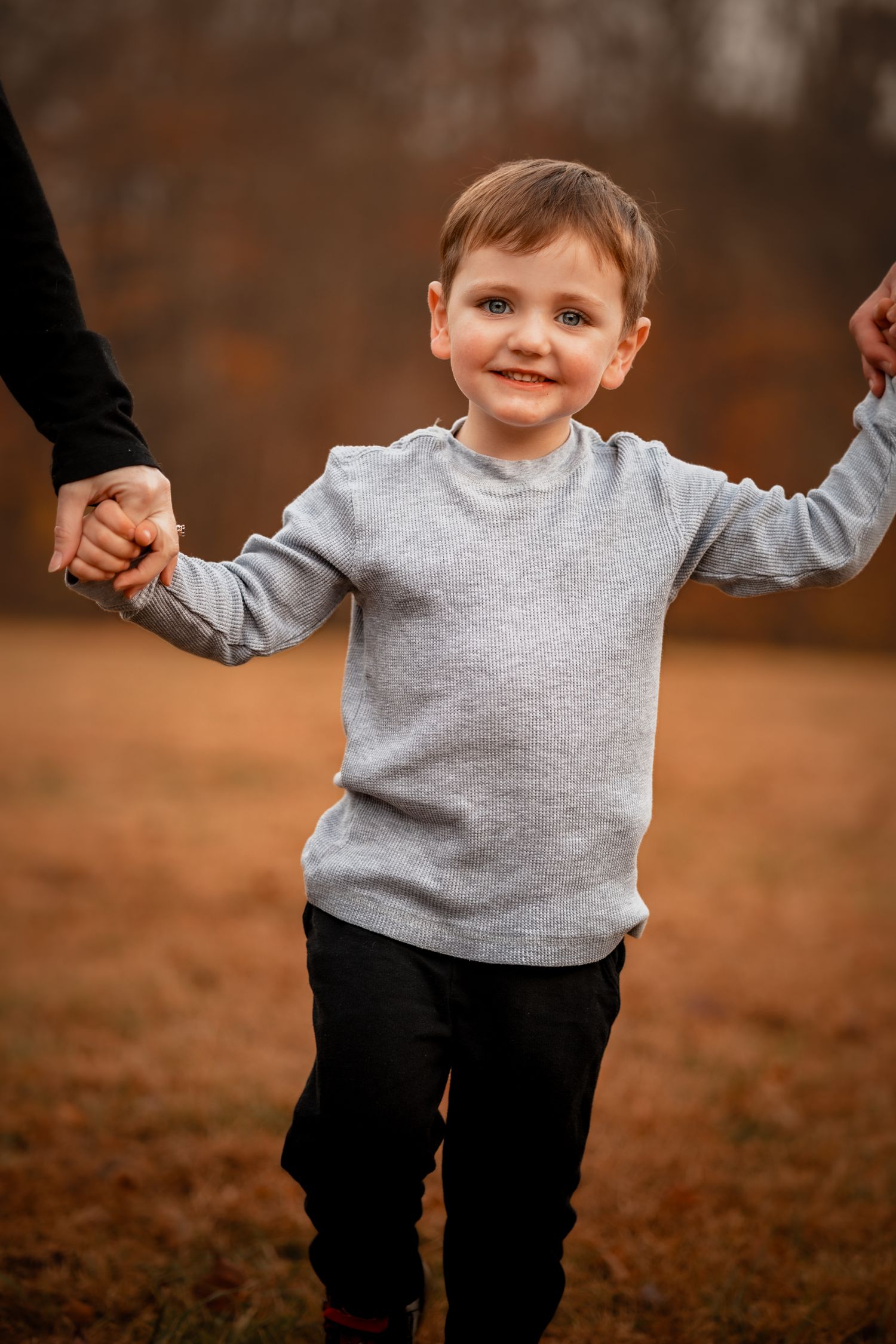 Child in grey sweater and dark pants playing outdoors on autumn day.